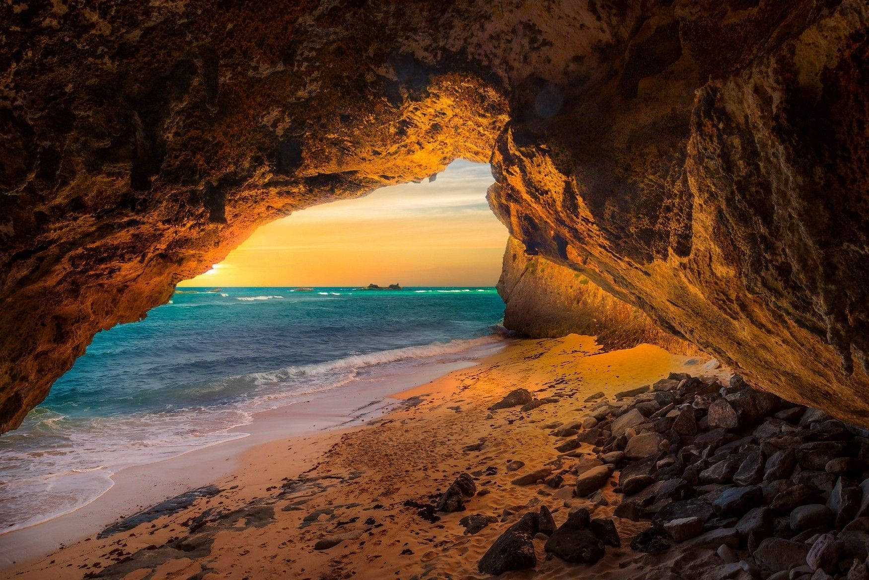 土克島與開曼群島的洞穴 壁紙 — 金色夕陽穿過天然岩石拱門，照耀在碧綠海洋沙灘、沙灘和散落的石頭上。