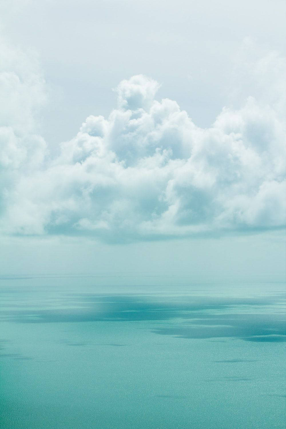 土克島與開曼群島雲景 壁紙 — 廣闊的藍綠色海洋在蒼白的天空下與柔軟的白雲相遇，呈現寧靜的空中景觀。