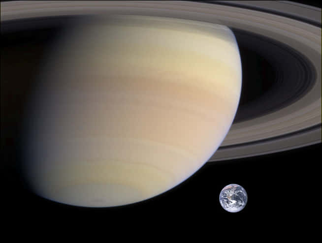 土星與地球比較 壁紙 — 土星以其標誌性的環主導畫面，一顆小小的藍色地球在廣闊的太空黑暗中漂浮在附近。