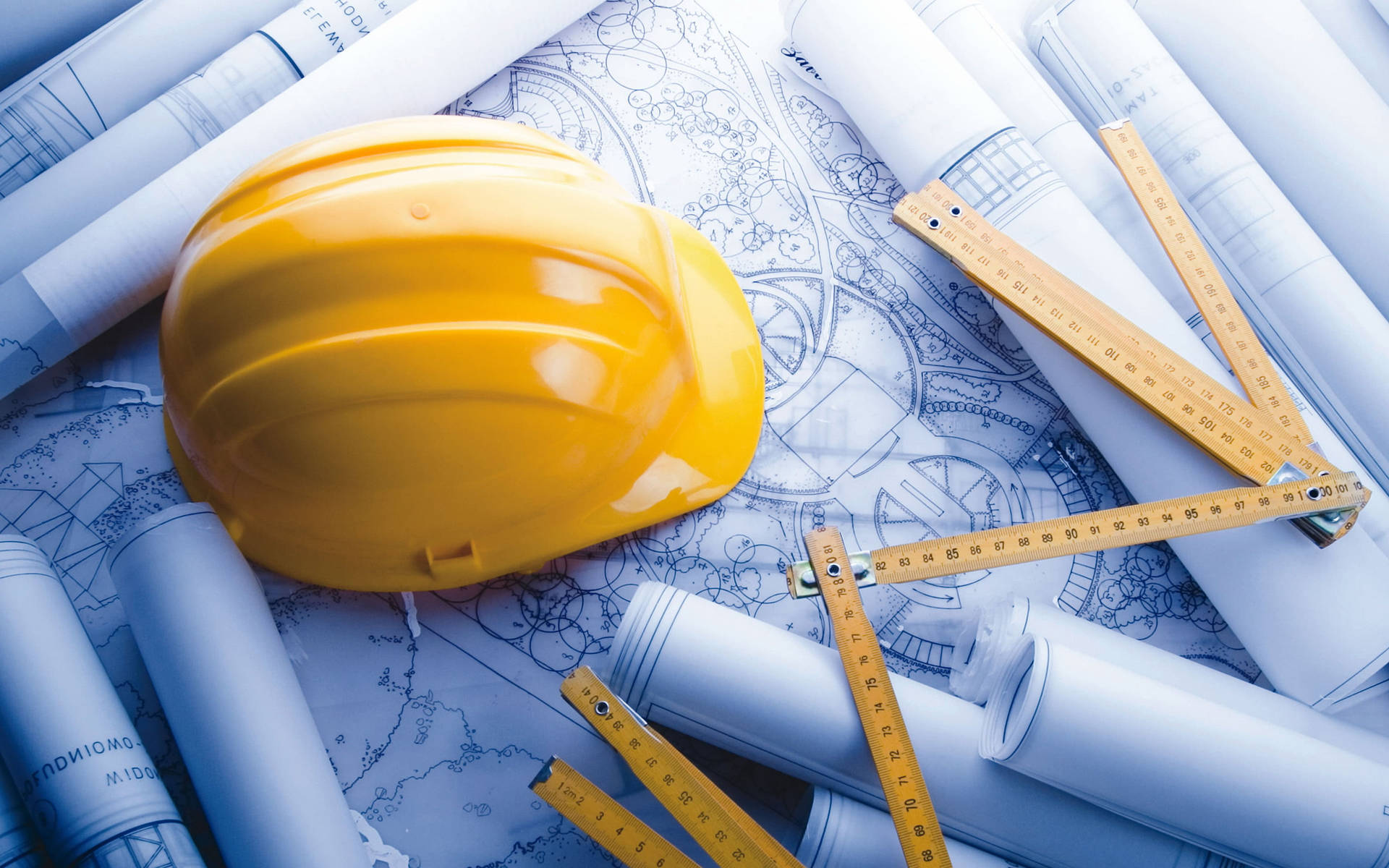 黃色安全帽和測量工具放在捲起的藍圖上，用於建築規劃。