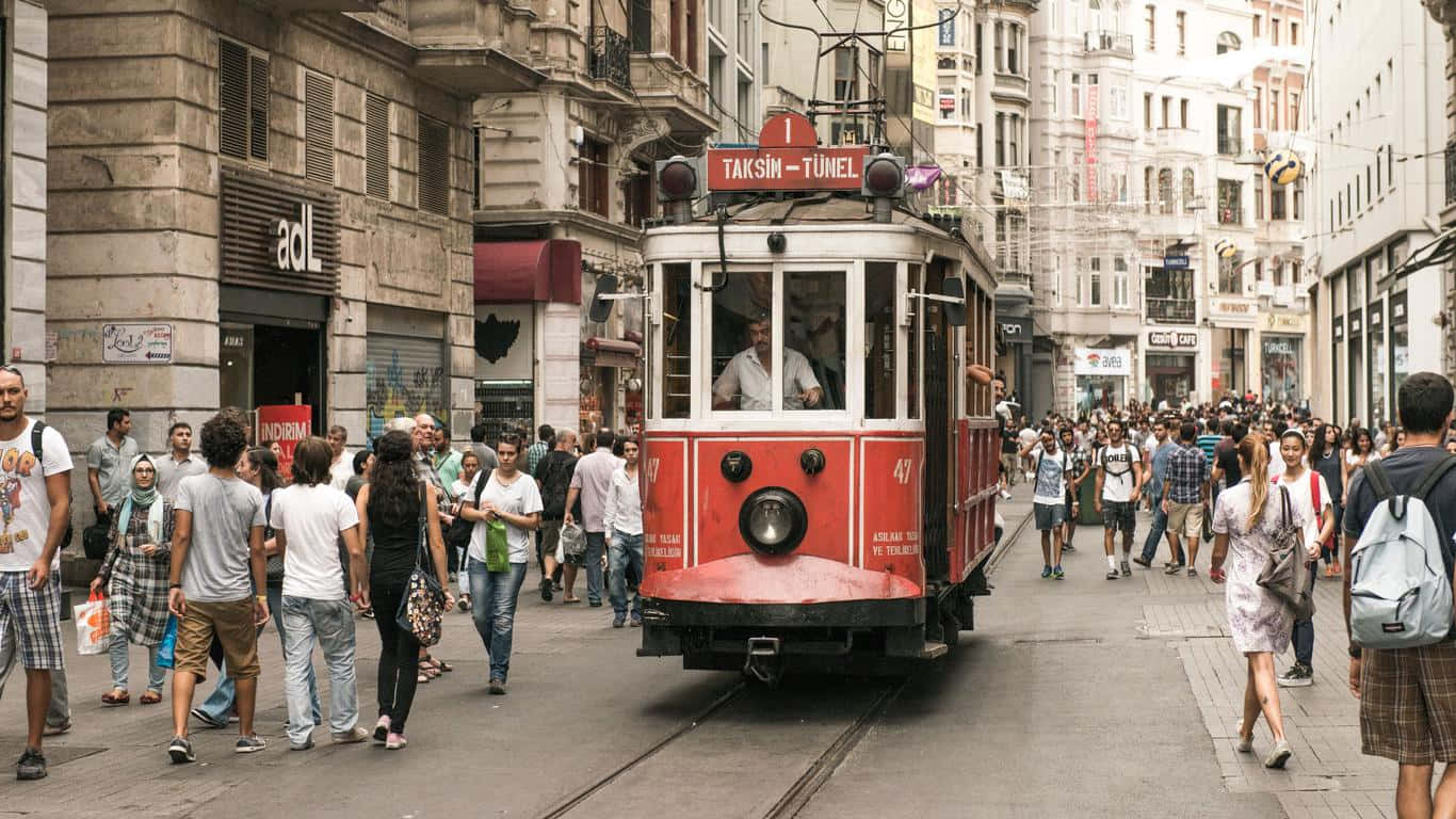 土耳其卡帕多奇亞的迷人風景 壁紙 — 一輛紅色復古電車，標有Taksim-Tunel，穿梭於一條擠滿行人和歷史建築的繁忙狹窄街道。