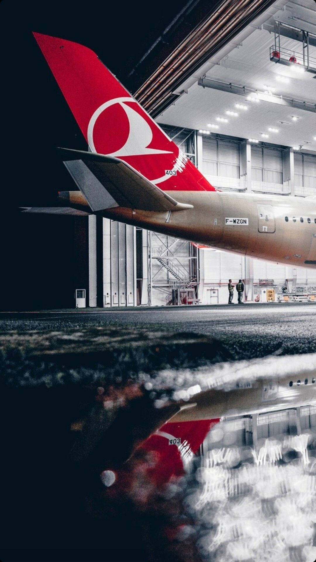 土耳其航空飛機尾部倒映在機庫內水坑中，兩人。