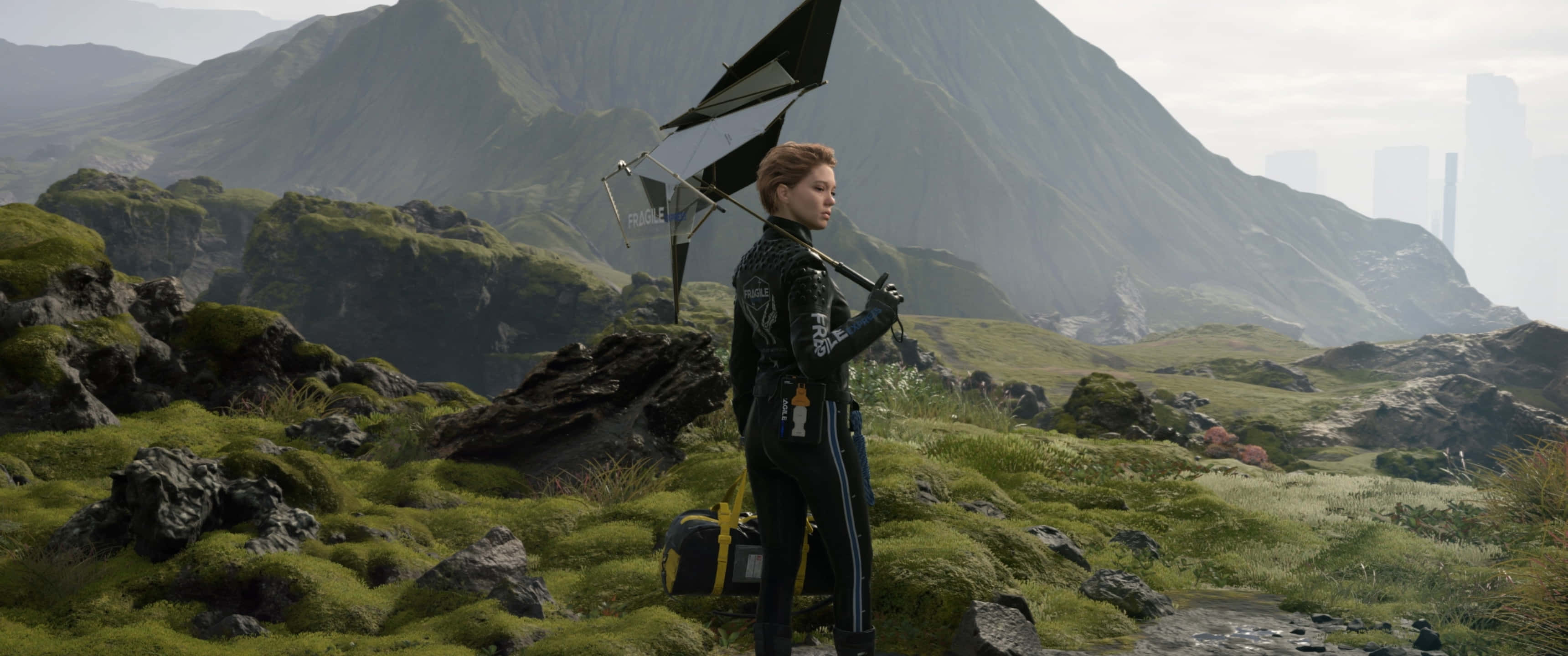在 3440x1440p 解析度下體驗《死亡擱淺》 壁紙 — 一名身穿黑色賽車服的女士站在長滿苔蘚的岩石山坡上，手持一面黑色小帆，遠處可見未來主義的城市天際線。