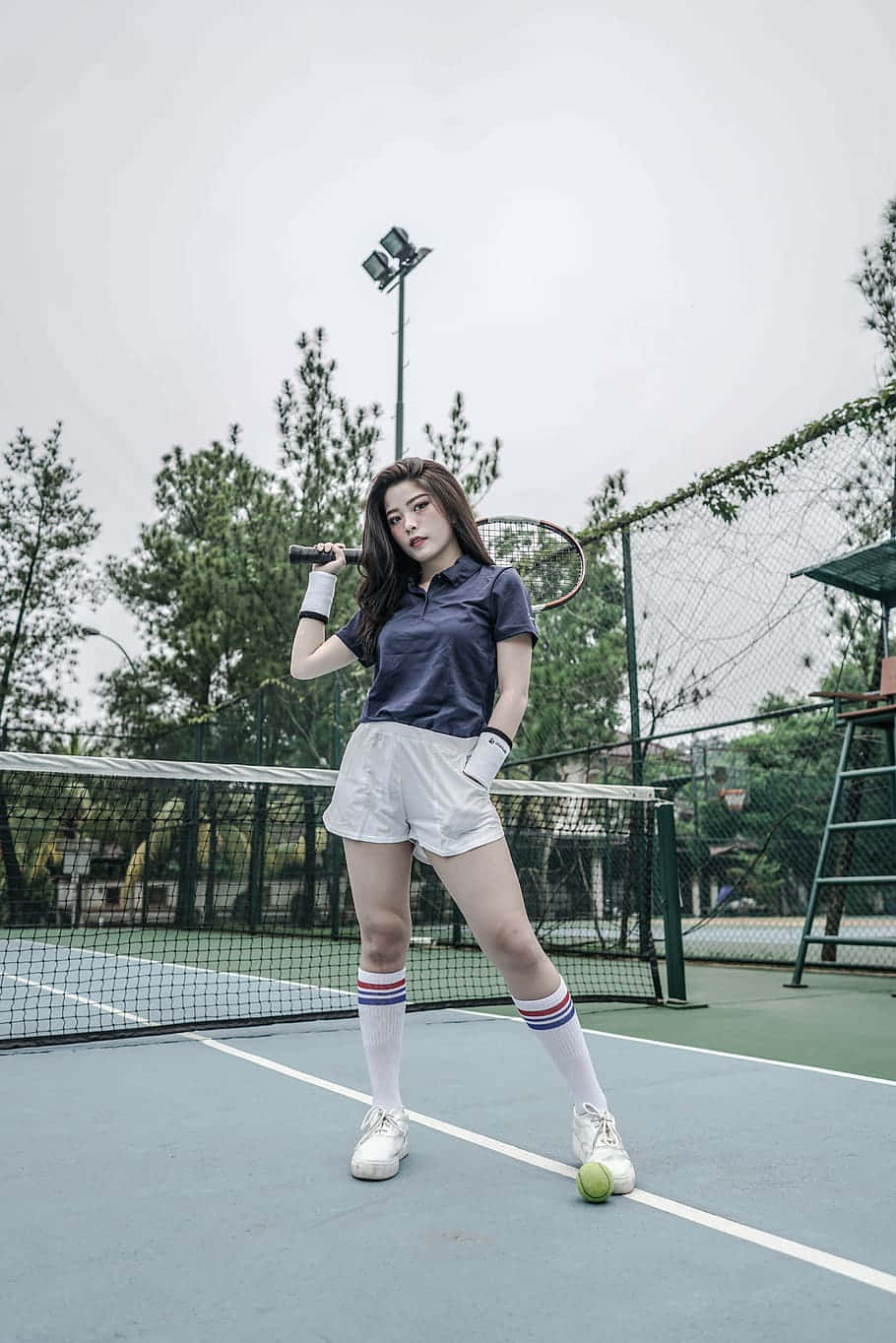 年輕女子穿著網球服裝在球場上擺姿勢，手持球拍和球。