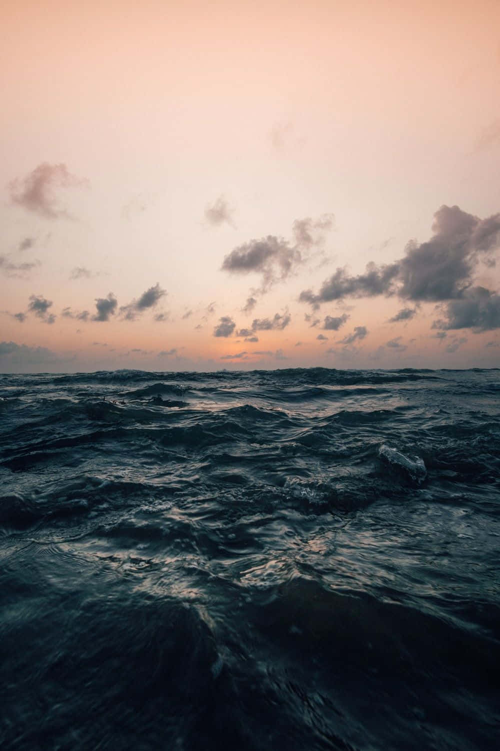 日落時分的海浪，粉紅和橙色天空，散落的雲朵。