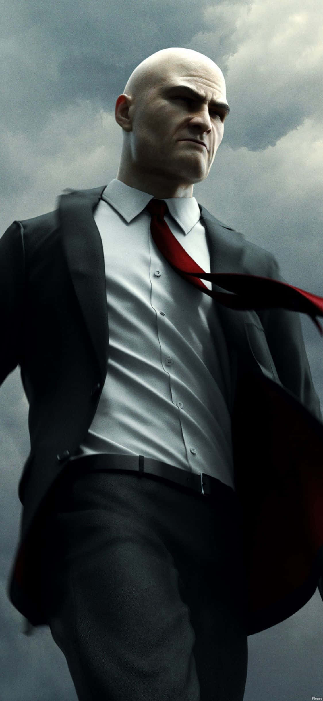 在 iPhone X 上體驗《Hitman Absolution》 壁紙 — 一個光頭男子穿著黑色西裝和紅色領帶，在暴風雨的灰色天空下，表情嚴肅地站立。