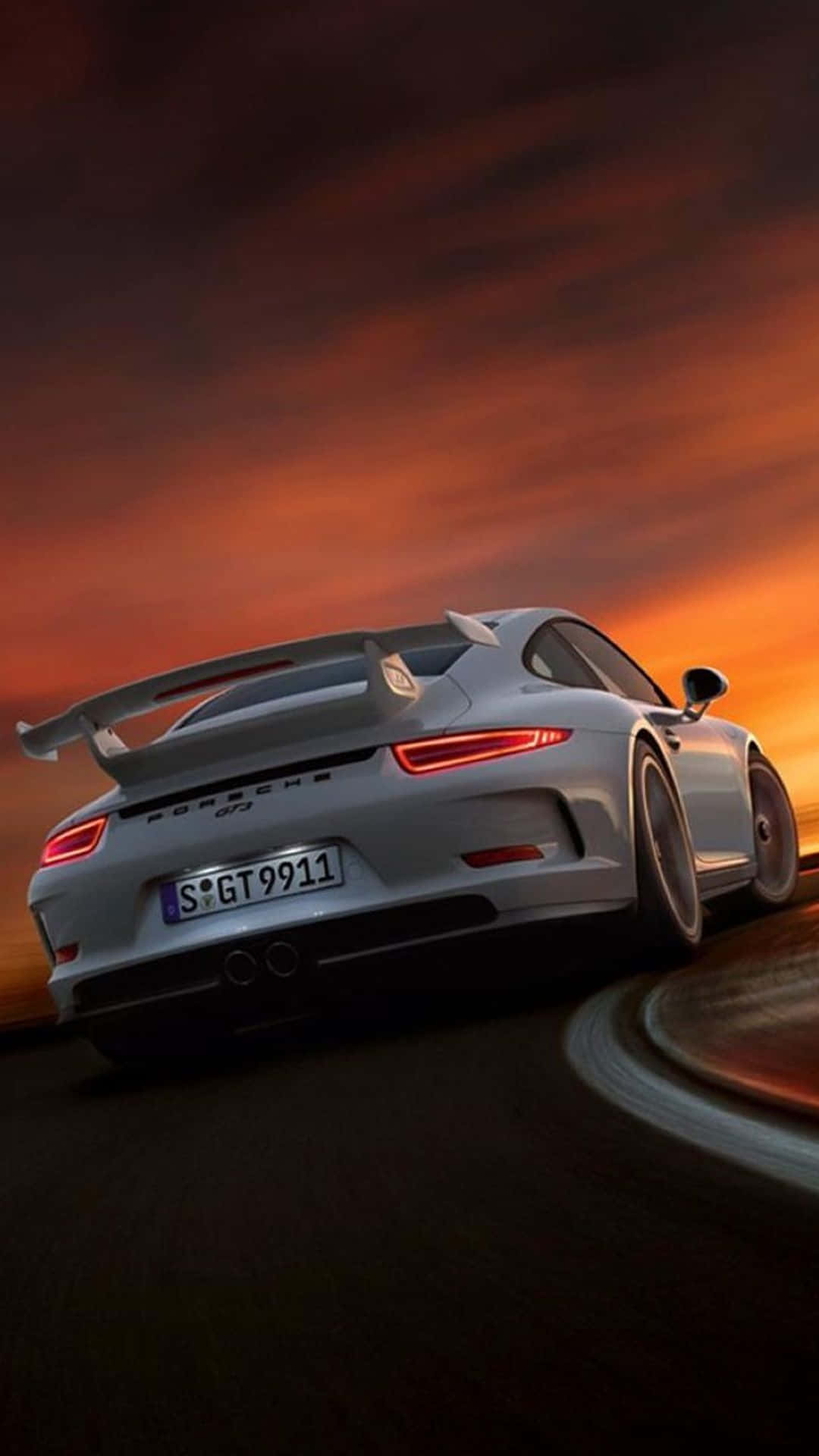 在 iPhone XS Max 上駕駛《Project CARS 2》，感受尖端賽車體驗 壁紙 — 一輛銀色保時捷911 GT3在蜿蜒的道路上行駛，天空是火紅橙色的日落。