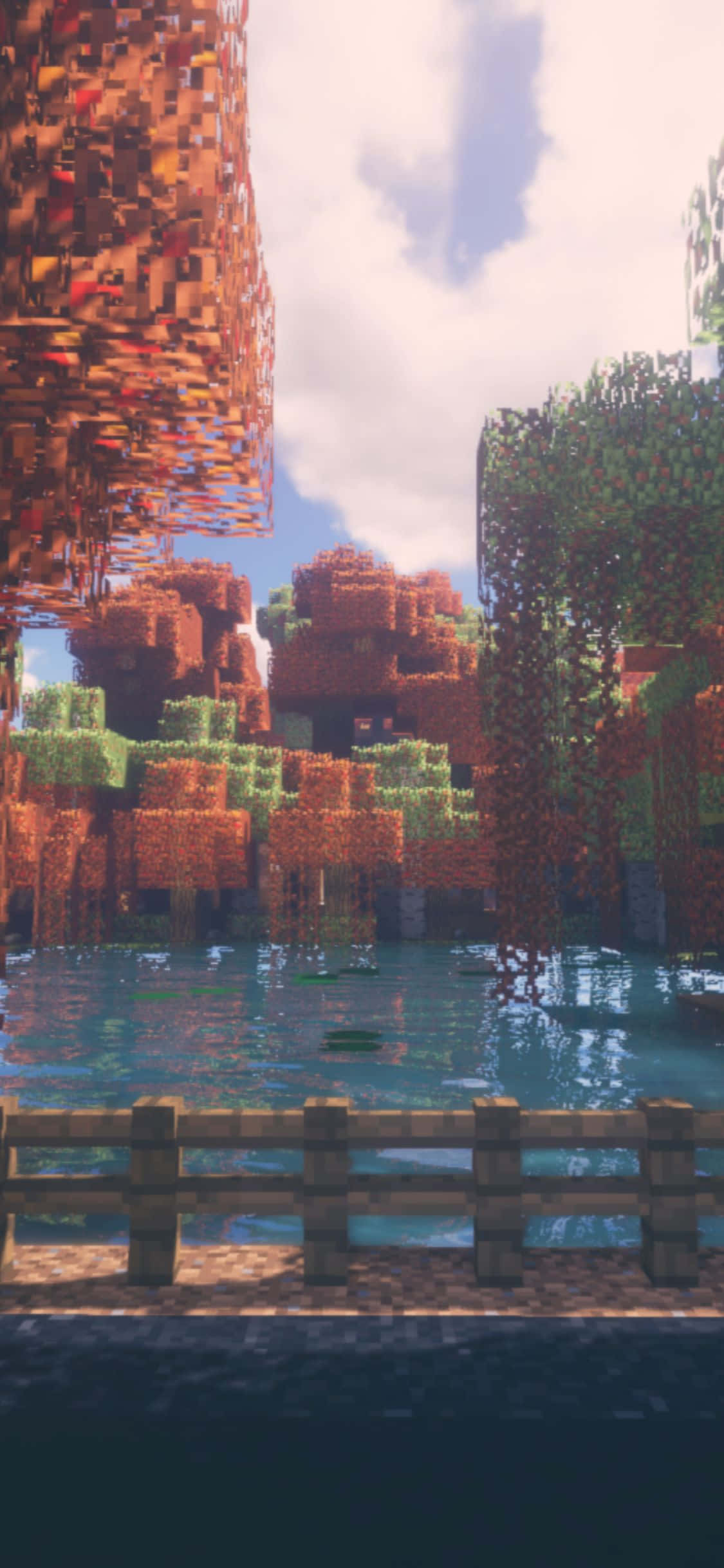 在 iPhone Xs 上，Minecraft 帶來無限探索世界 壁紙 — 一個像素化的Minecraft景觀，有橙色方塊樹木和綠色樹葉，在明亮的天空下倒映在平靜的藍色水中。