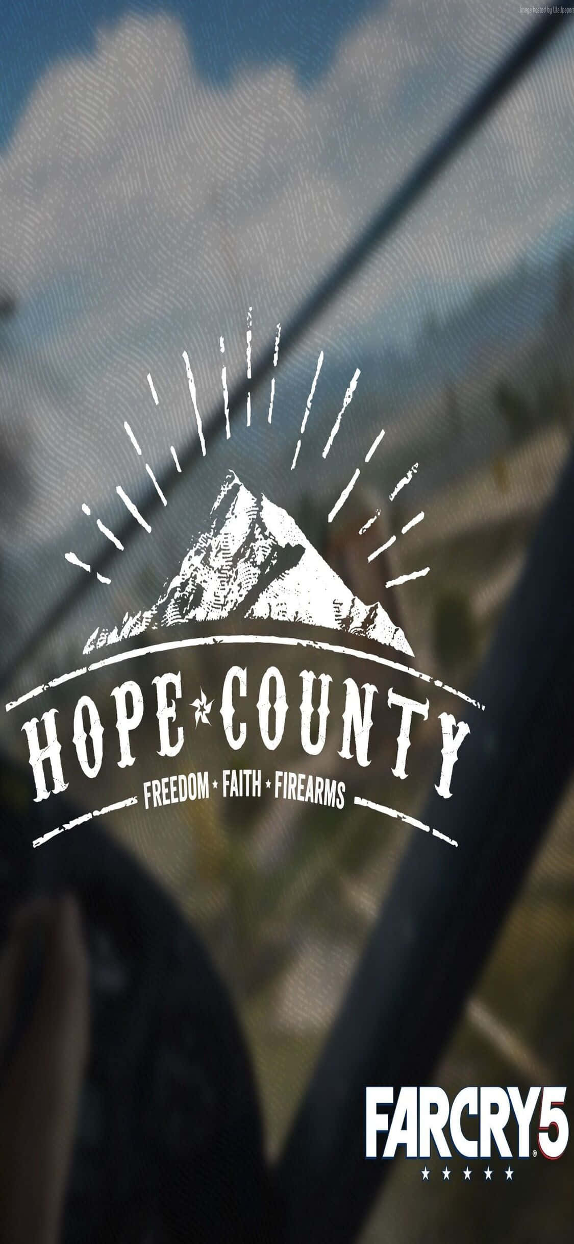 在 iPhone Xs 上體驗《孤島驚魂5》的強大性能 壁紙 — 一個白色的Hope County標誌，帶有山脈和太陽爆發圖形，疊加在透過車窗看到的模糊景色上。