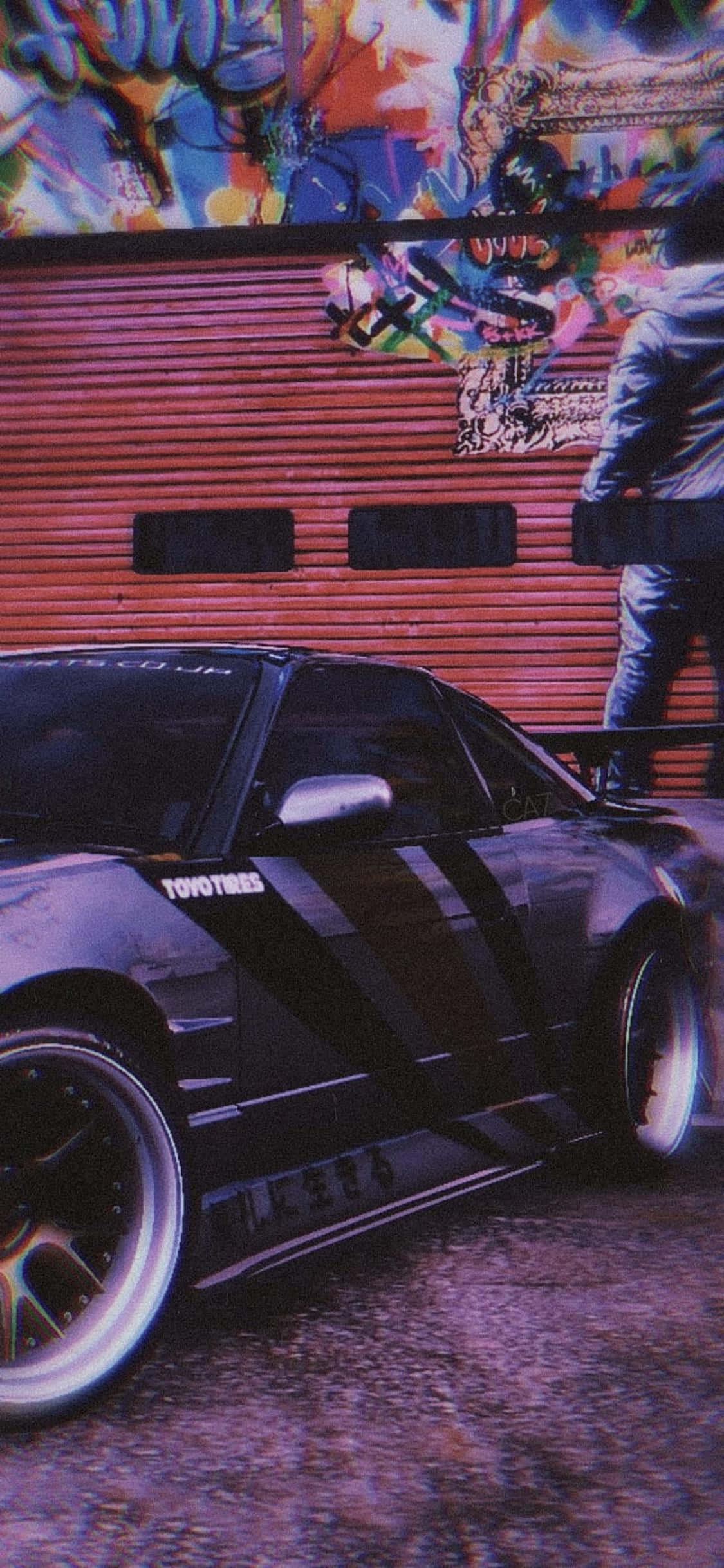 在 iPhone XS 上體驗《Need for Speed Heat》的極速快感 壁紙 — 一輛帶有Toyo Tires貼紙的黑色改裝跑車停在塗鴉覆蓋的紅色車庫門前，附近站著一個人。
