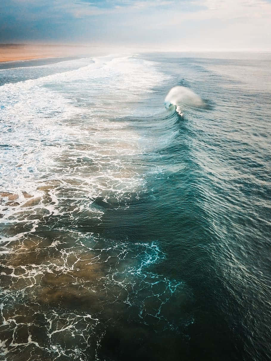 從空中拍攝，一道巨大的海浪在沙灘附近破碎，泛起白色泡沫。