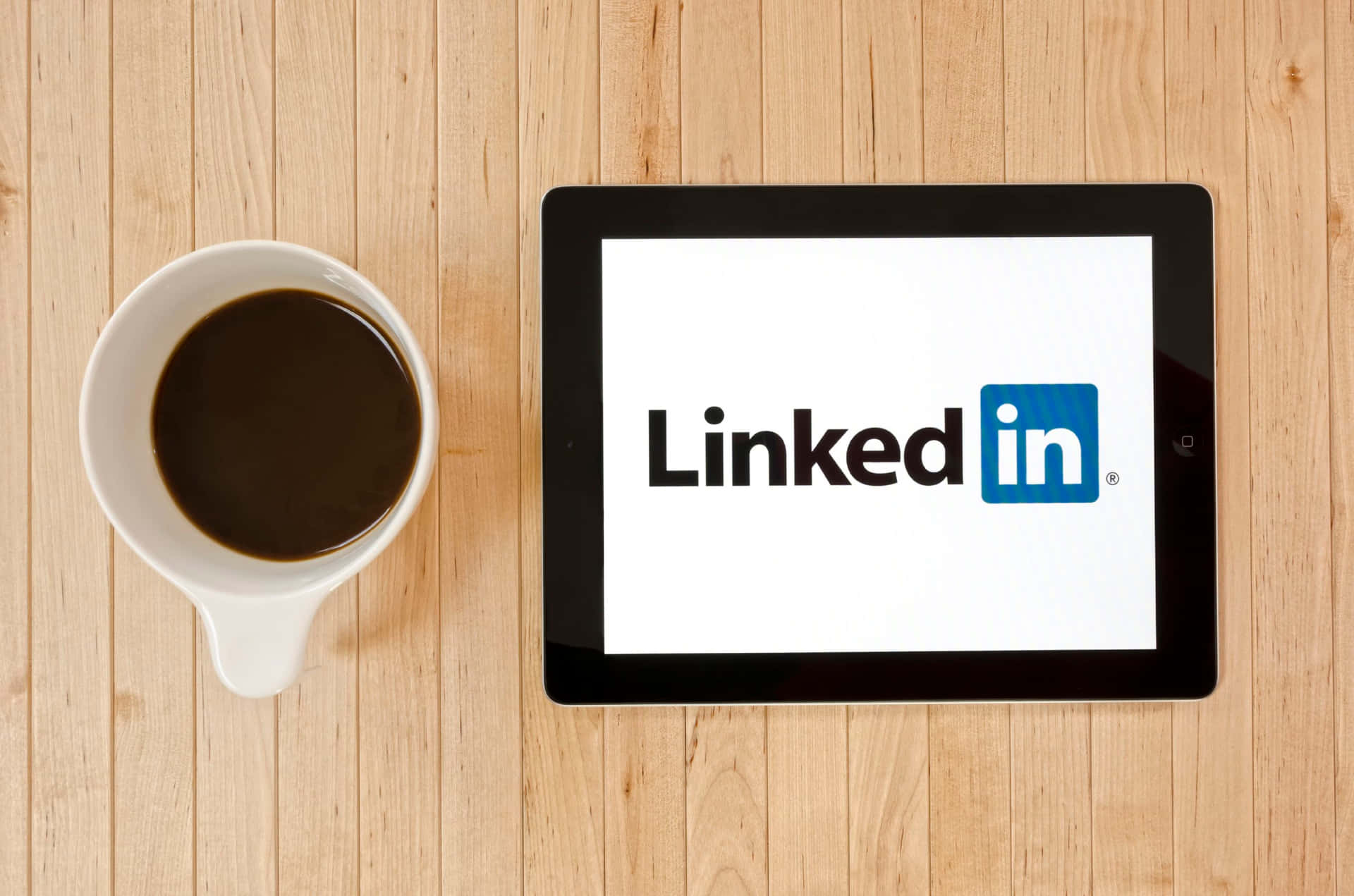 平板電腦顯示LinkedIn標誌，旁邊有咖啡杯在木桌上。