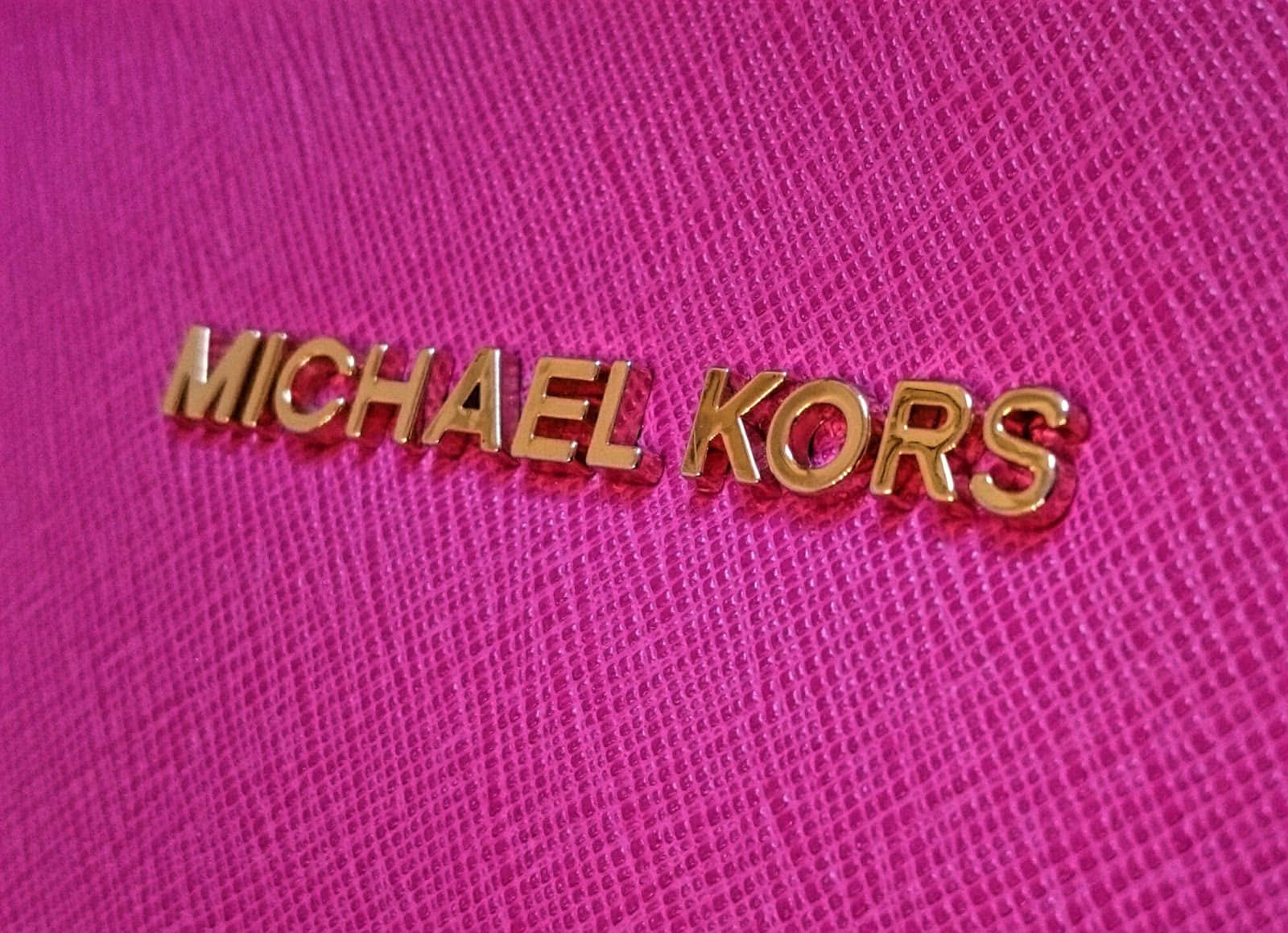 金色Michael Kors標誌在紋理粉紅色布料上。