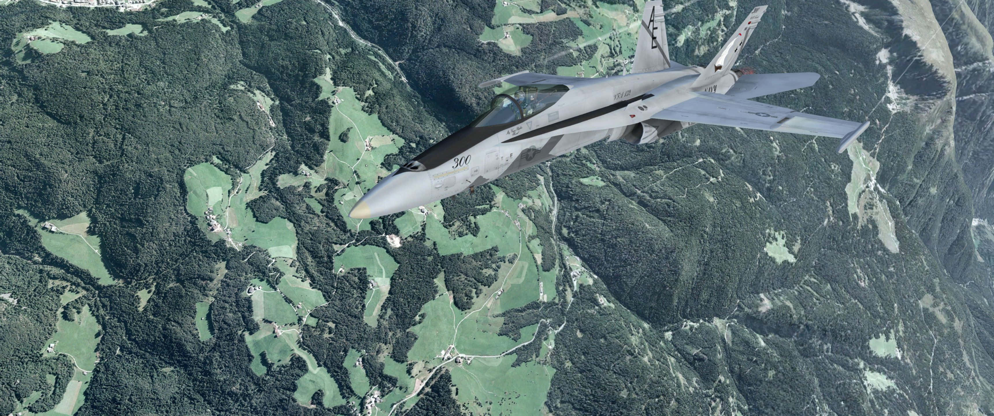 在 Microsoft 飛行模擬器中飛入雲層 壁紙 — 一架流線型灰色戰鬥機在鬱鬱蔥蔥的綠色山區地形上空翱翔，下方是蜿蜒的山谷。