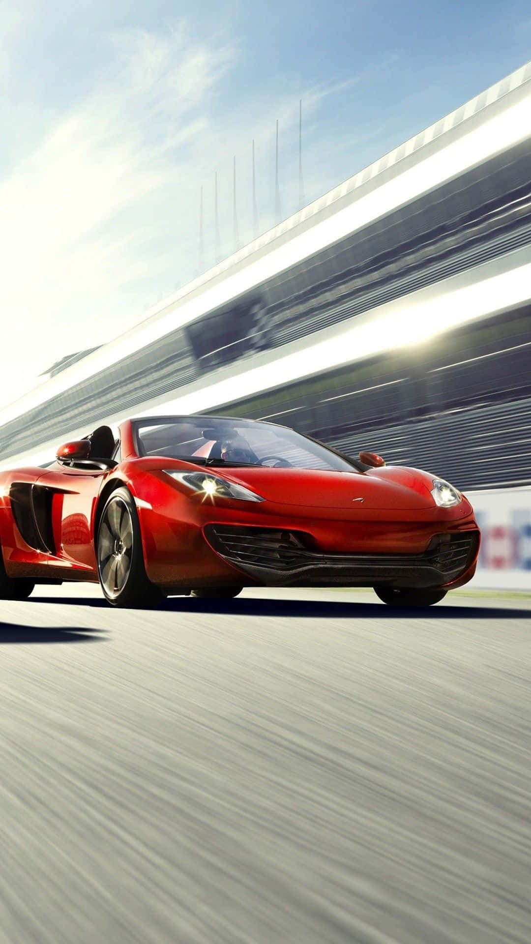 在《Need for Speed Heat》中夜間疾馳 壁紙 — 一輛充滿活力的紅色跑車在明亮的藍天下沿著賽道飛馳，動態模糊強調了速度。