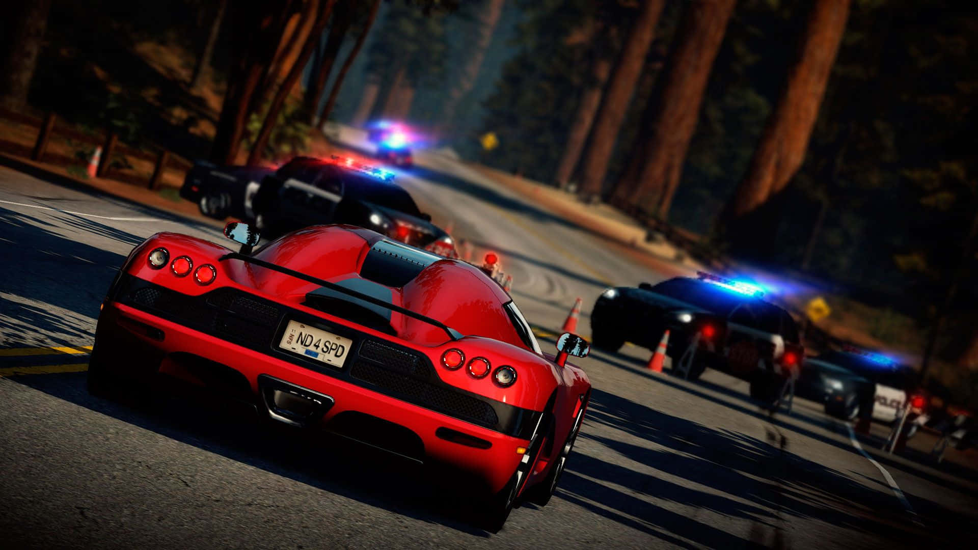 在《Need for Speed》中夜間狂飆 壁紙 — 一輛紅色跑車在黃昏時分沿著森林道路疾馳，後面有閃著警燈的警車追趕。