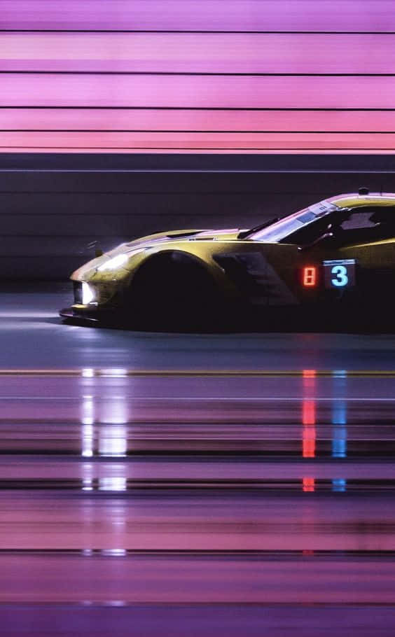 在 Pixel 3 Grid Autosport 中體驗沉浸式賽車快感 壁紙 — 一輛金色賽車在霓虹燈下疾馳而過，紫色和粉紅色的條紋照亮了潮濕的賽道。