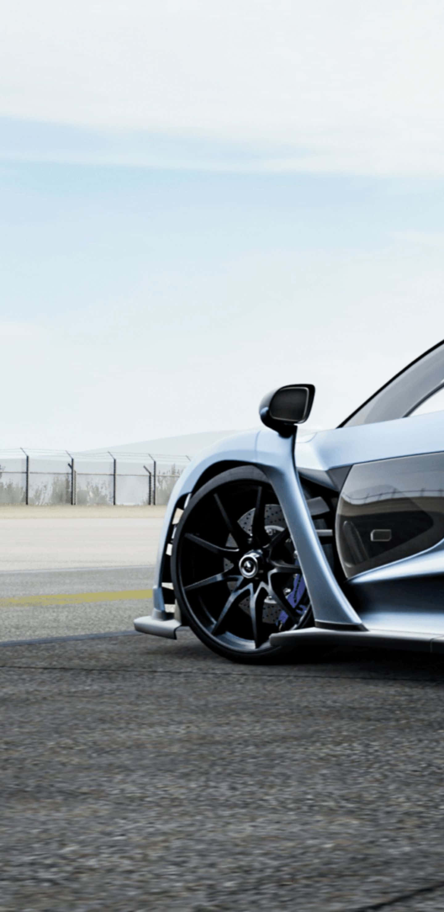 在 Pixel 3 XL 上完全沉浸於 Forza Motorsport 7 的刺激賽車世界 壁紙 — 一架時尚的銀色跑車，配備黑色輪圈和藍色制動卡鉗，停泊在灰濛天空下的瀝青賽道上。