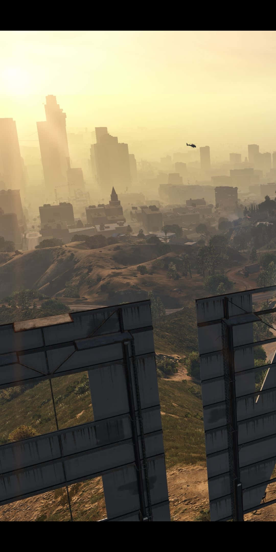在 Pixel 3 上體驗《GTA V》的非-stop 高能畫面 壁紙 — 朦朧的金色日出沐浴著廣闊的城市景觀，高聳的摩天大樓和遠處的直升機飛越起伏的山丘。