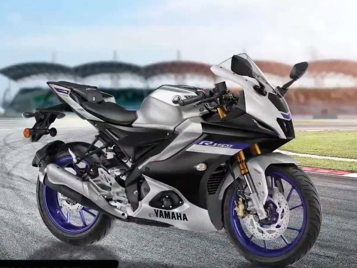 在 R15 上探索無限潛能 壁紙 — 一架時尚的銀色和黑色Yamaha R15V3電單車，配紫色輪圈，在明亮的天空下停在賽道上。