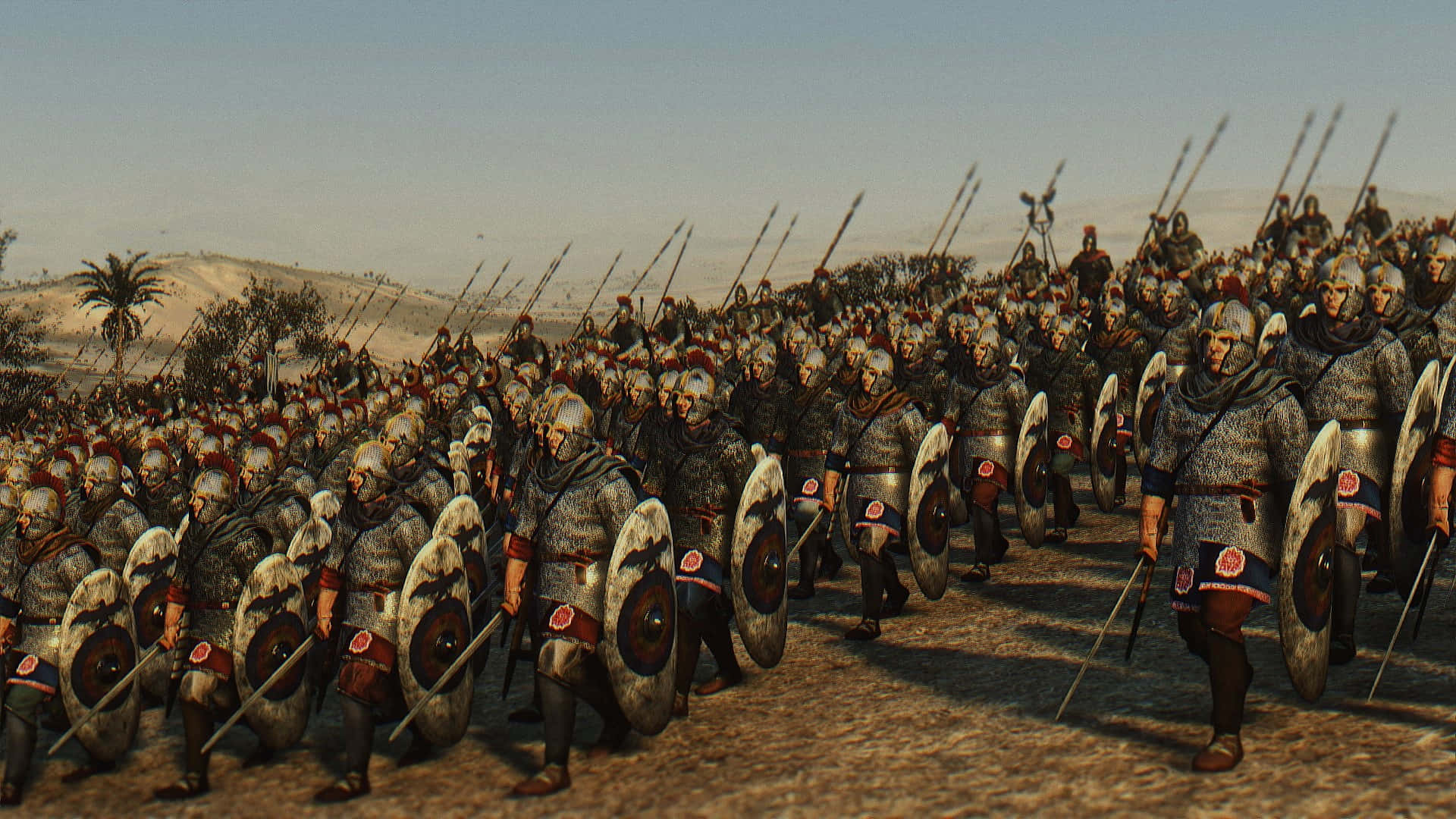 在《TOTAL WAR ROME II》中征服全球 壁紙 — 大批全副武裝的羅馬軍團士兵在蒼白的天空下，以緊密隊形行進在陽光明媚的沙漠平原上。