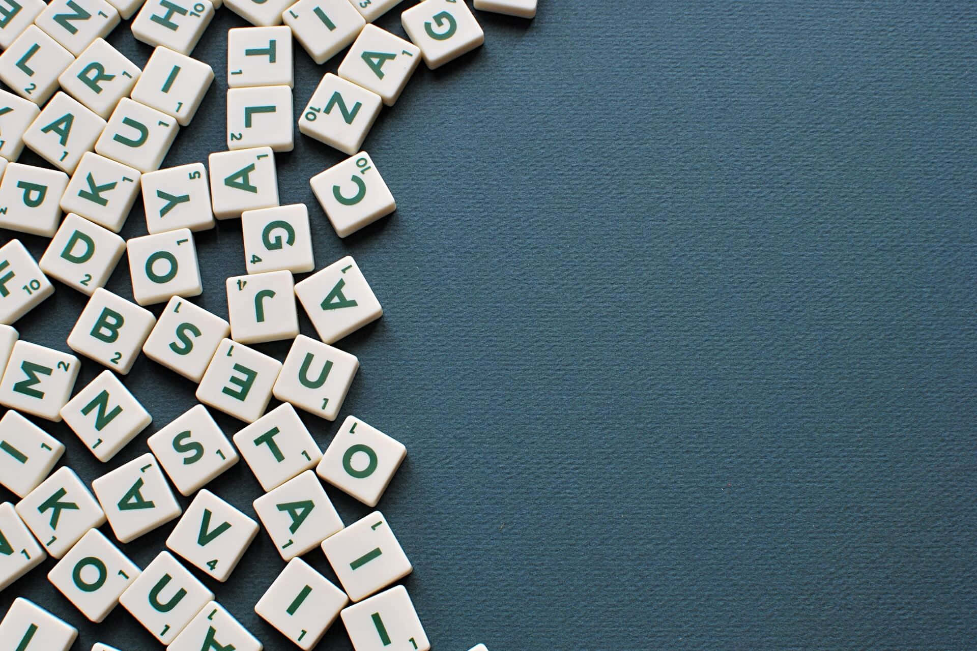 在 Word 中工作 壁紙 — 白色 Scrabble 瓷磚，帶有綠色字母，對角散落在有紋理的青綠色表面上。