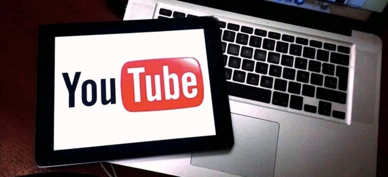 👩💻 在 YouTube 玩得開心 壁紙 — 一部顯示YouTube標誌的平板電腦放在木桌上的一部銀色筆記型電腦鍵盤上。