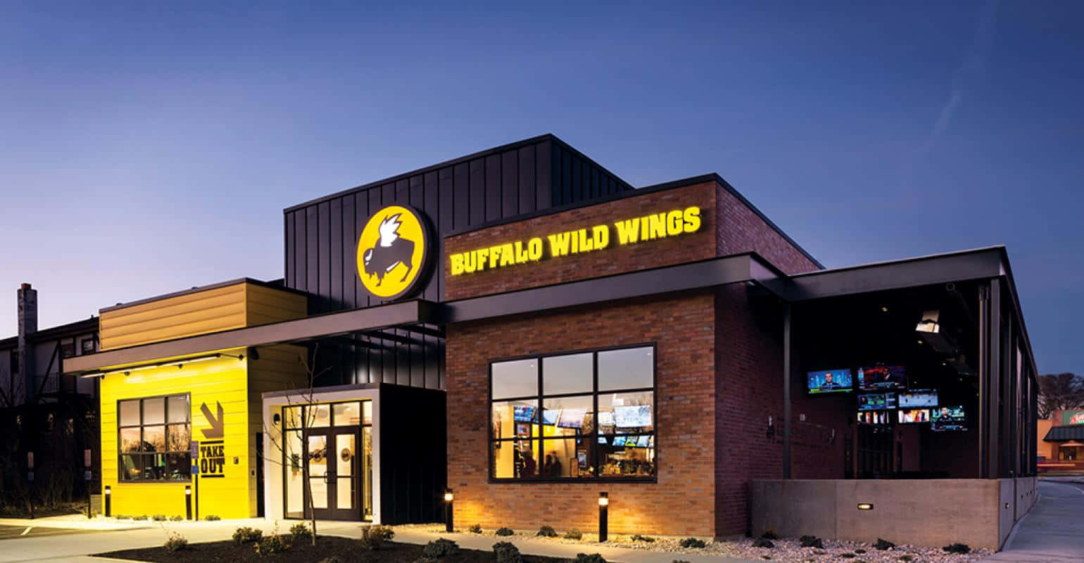 Buffalo Wild Wings 餐廳外部在黃昏時分亮起，帶有發光的黃色招牌和磚砌外牆。