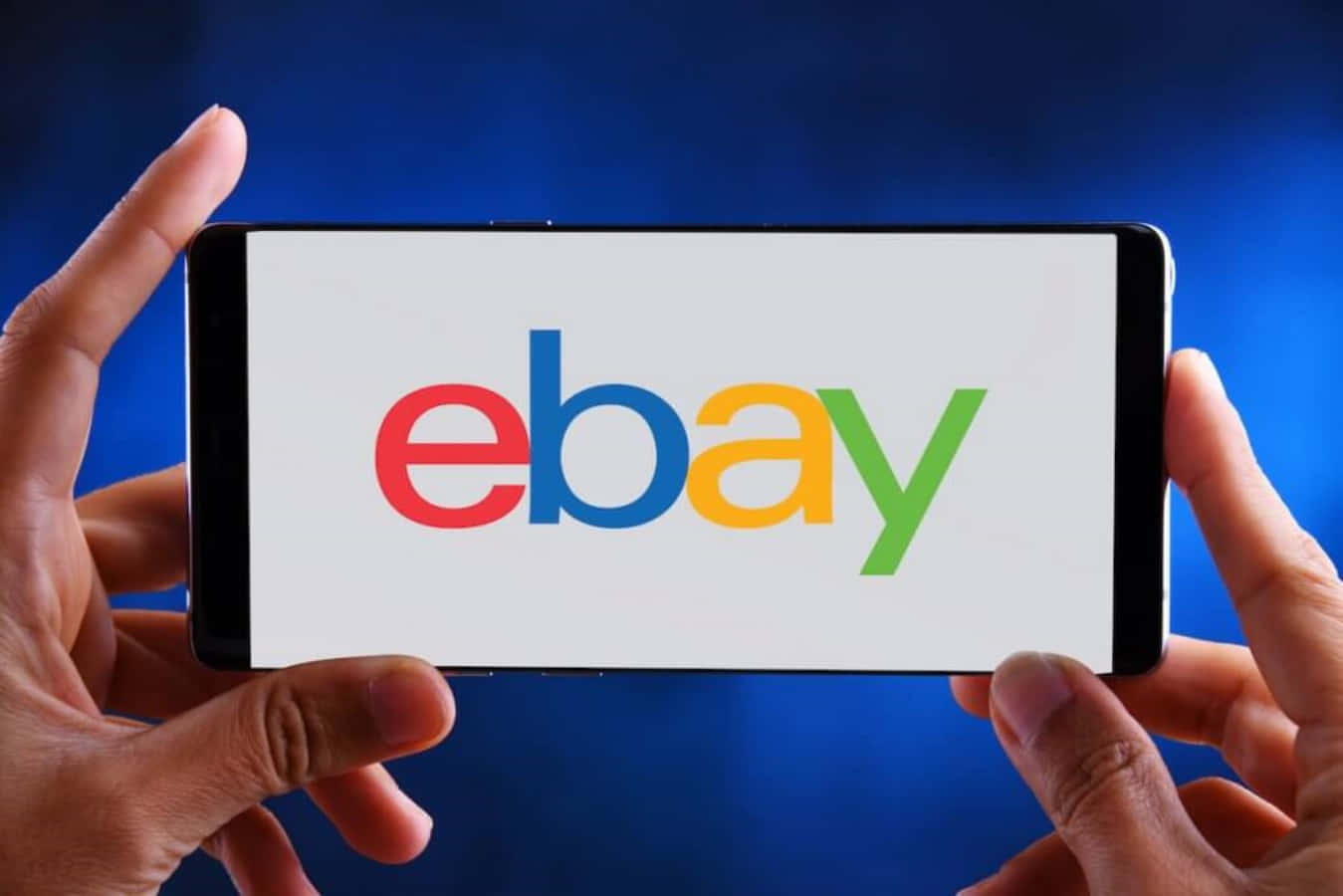 手拿著一部在藍色背景上顯示eBay標誌的電話。