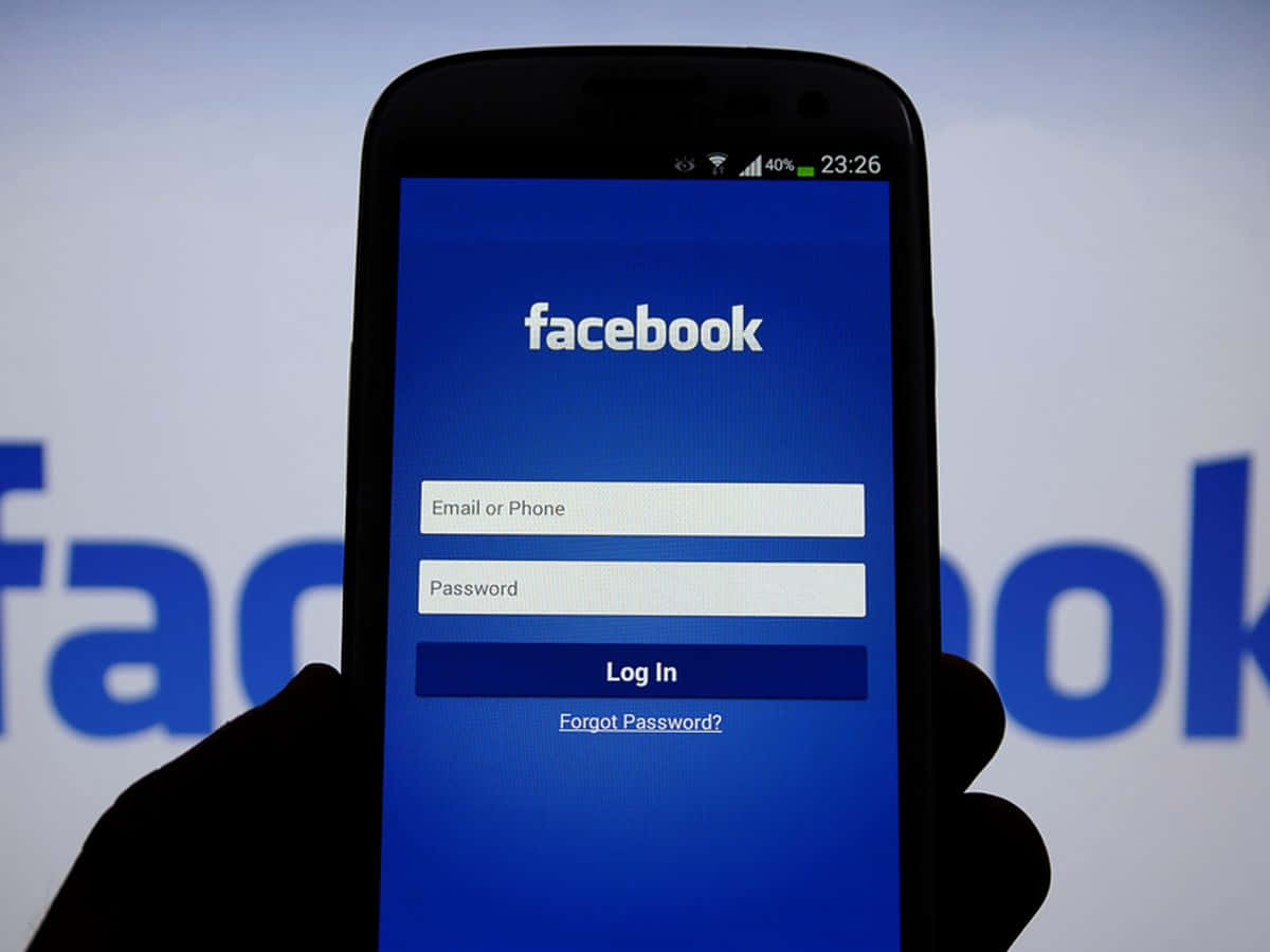 手拿著手機顯示Facebook登入畫面，背景有模糊標誌。