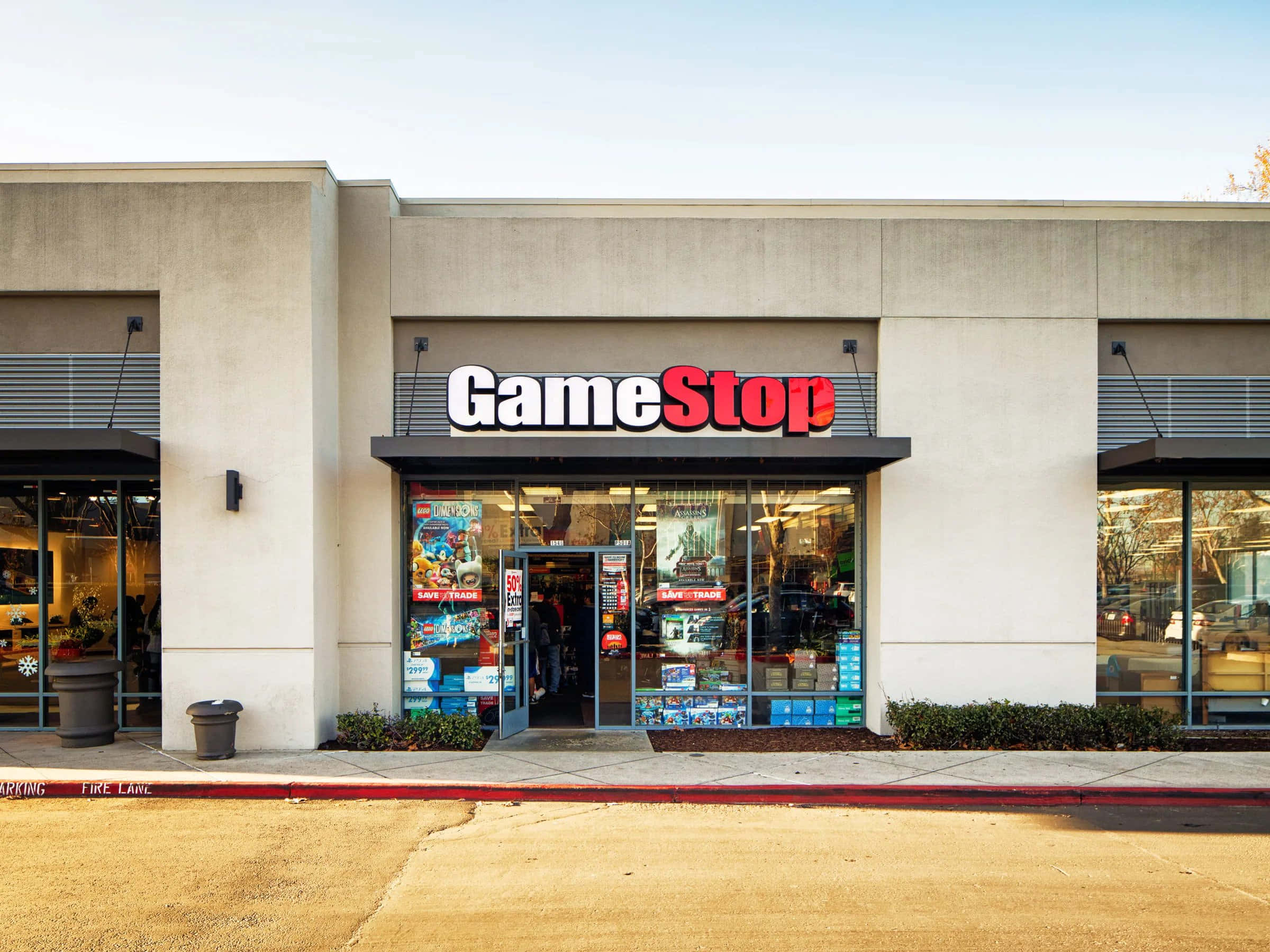 在Gamestop找到您的下一款最愛遊戲！ 壁紙 — 明亮的GameStop店舖正面，玻璃窗展示電子遊戲和商品，天空晴朗。