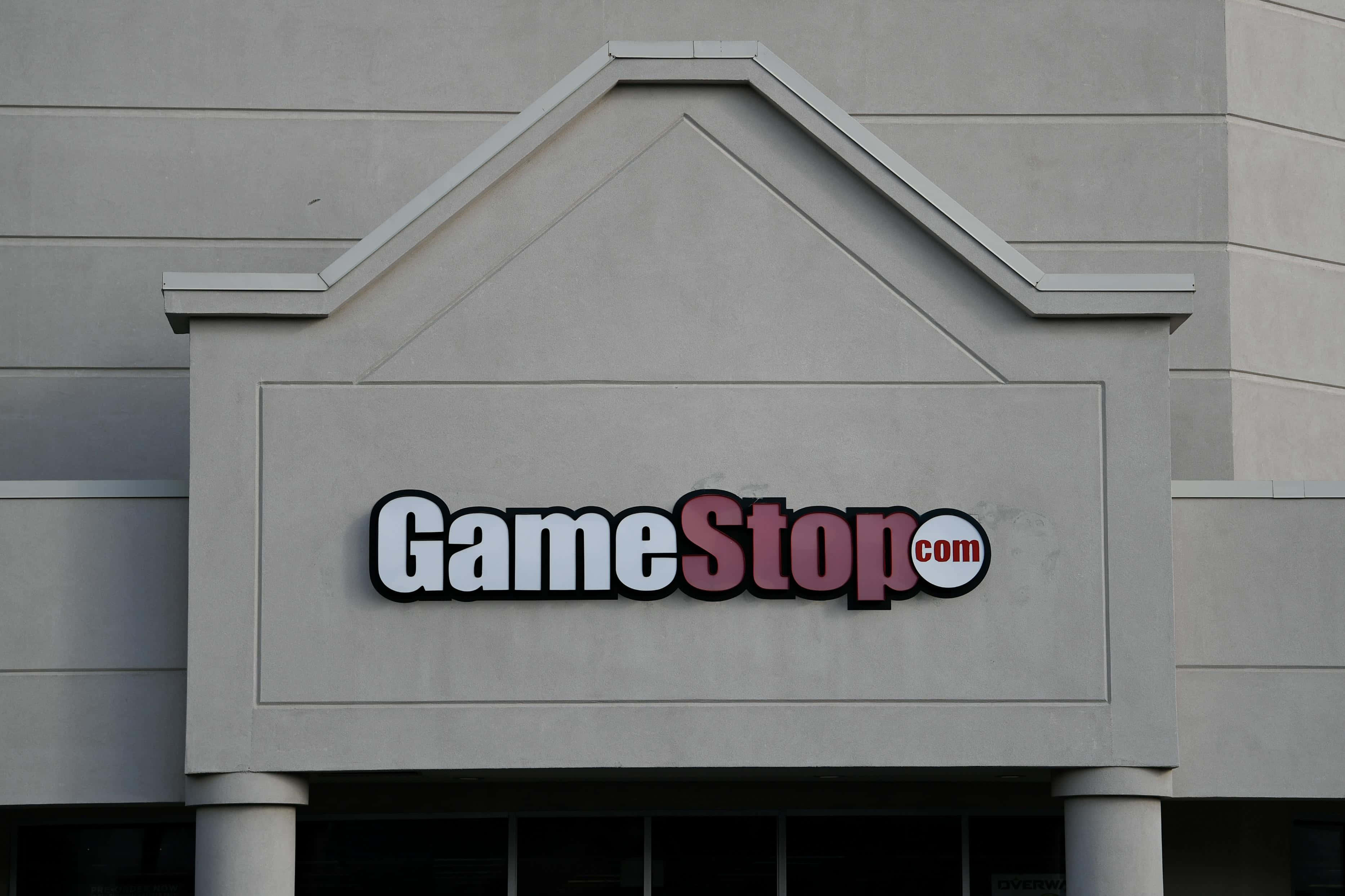 在GameStop購買您最愛的遊戲！ 壁紙 — 特寫鏡頭：在陰天之下，安裝在米色商業建築外牆上的GameStop.com商店招牌。