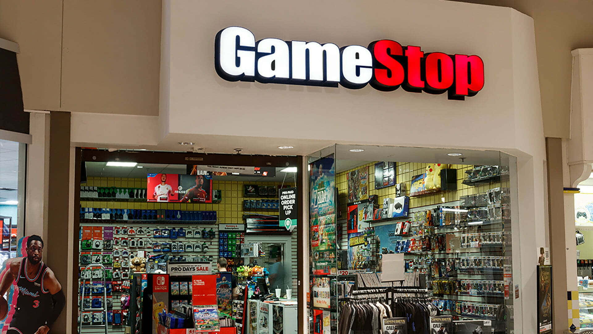 在GameStop購買最新遊戲 壁紙 — 光線明亮的GameStop店舖正面，玻璃門內可見貨架上擺滿了電子遊戲和商品。