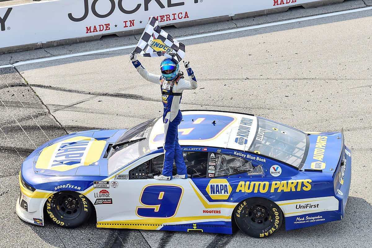 在NASCAR Sprint Cup Series賽事中衝向終點旗 壁紙 — 一位身穿藍白裝備的NASCAR車手站在他的藍黃色9號賽車上，在賽道上揮舞著方格旗。