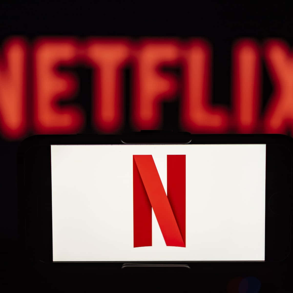 智能手機顯示 Netflix 標誌，背景有模糊的 Netflix 標牌。