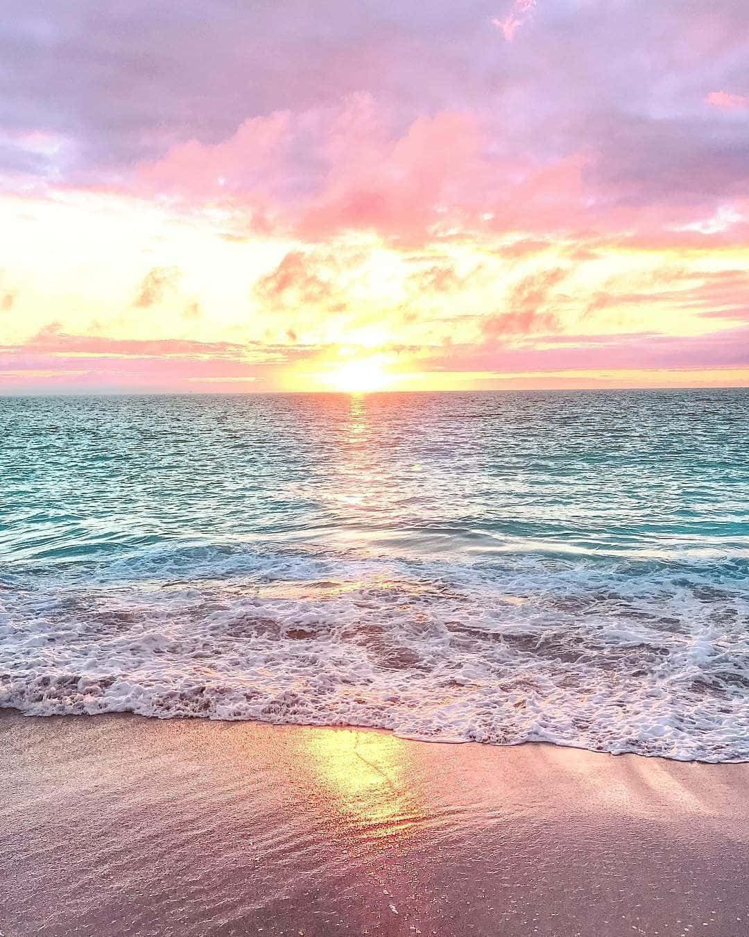 海洋上的夕陽，粉紅色和金色的天空映照在濕沙上。