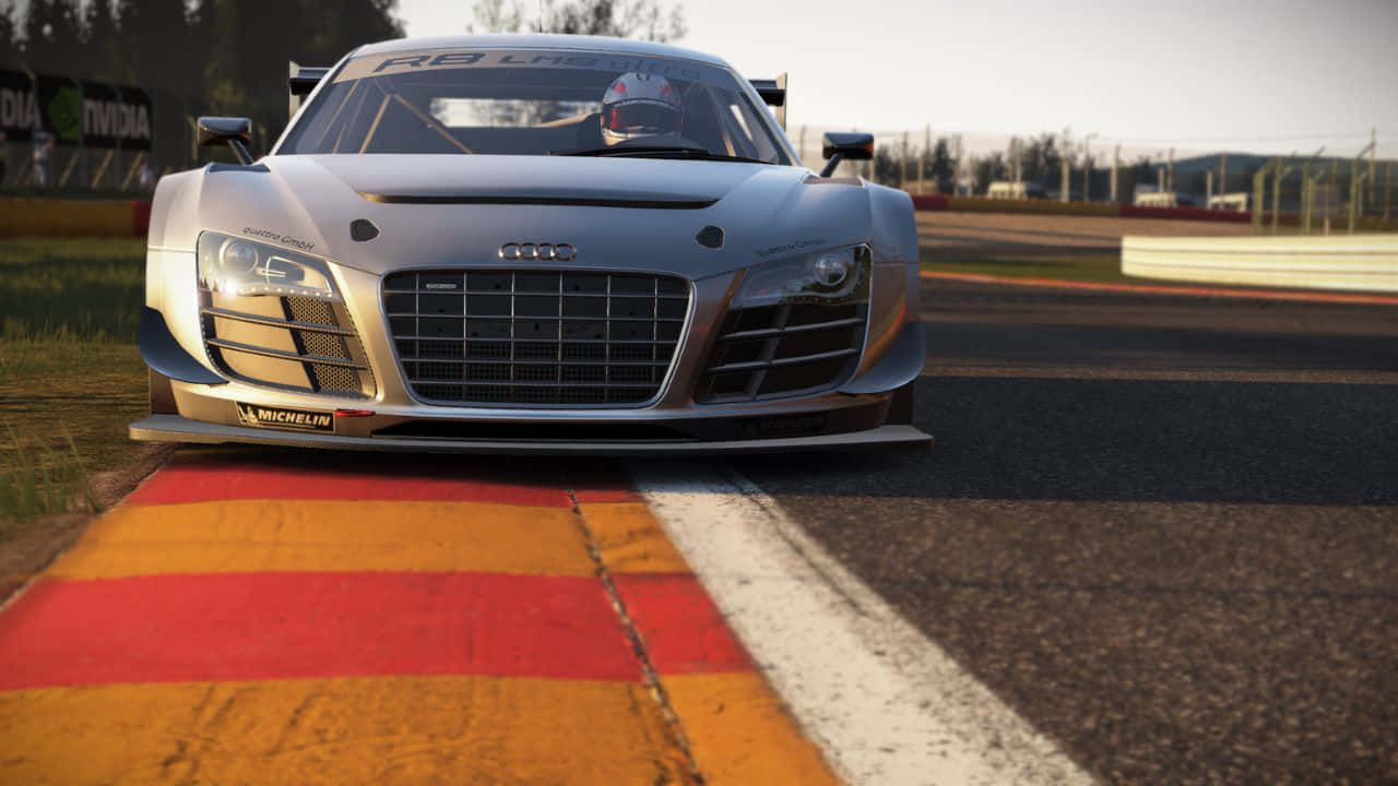 在Project Cars中衝向勝利！ 壁紙 — 一架時尚的銀色 Audi R8 LMS 賽車停在賽道邊緣，賽道上有紅色和黃色的路緣石，在溫暖的日光下。