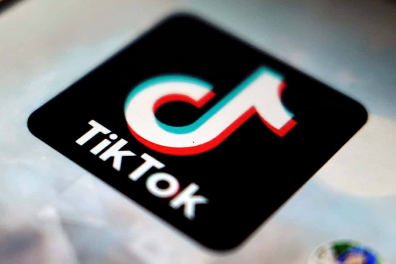 在TikTok上發揮創意，無限可能 壁紙 — TikTok應用程式圖標在模糊的智能手機屏幕上發出紅色、藍綠色和白色的特寫。