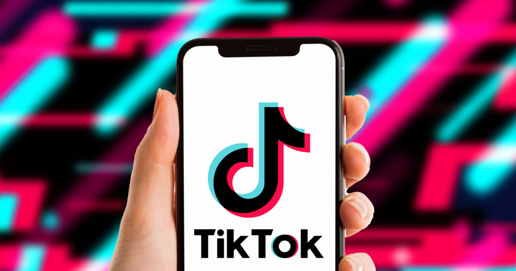 在TikTok上發揮創意，玩得開心！ 壁紙 — 一隻手拿著智能手機，顯示TikTok標誌，背景是充滿活力的霓虹抽象圖案。