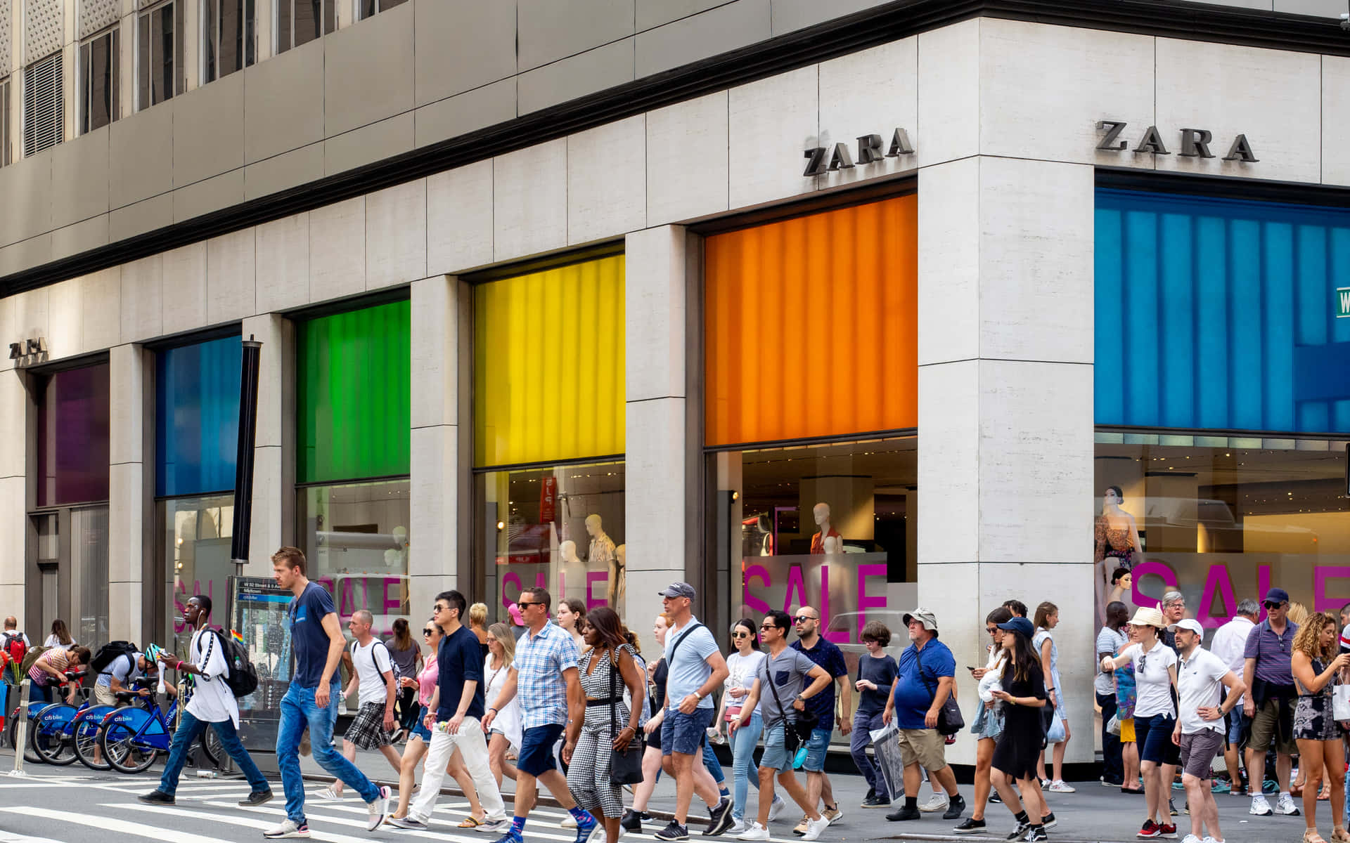 行人喺Zara商店前過馬路，商店有色彩繽紛嘅窗戶。