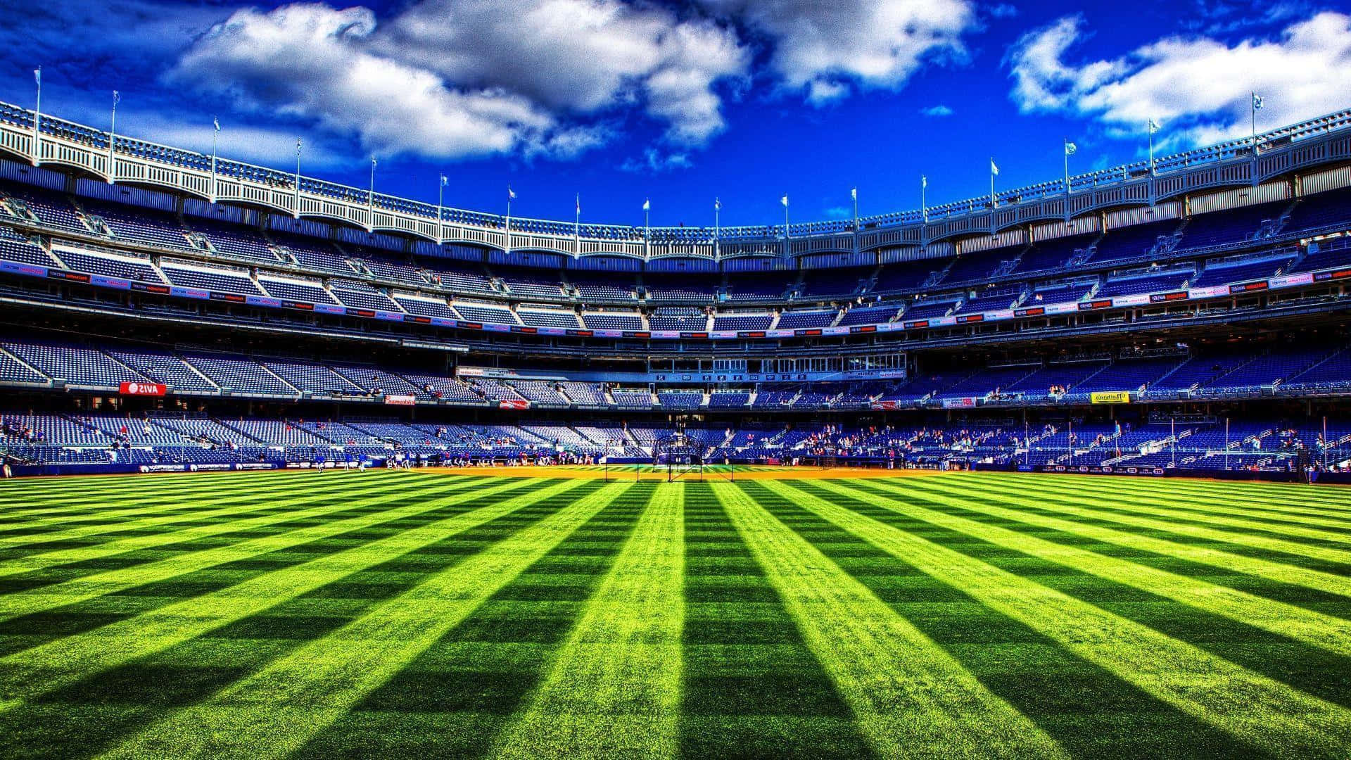 Cricket Ground 桌布 壁紙 — 在一個巨大的體育場內，明亮的藍天和蓬鬆的白雲下，充滿活力的綠色棒球場上有條紋草地。