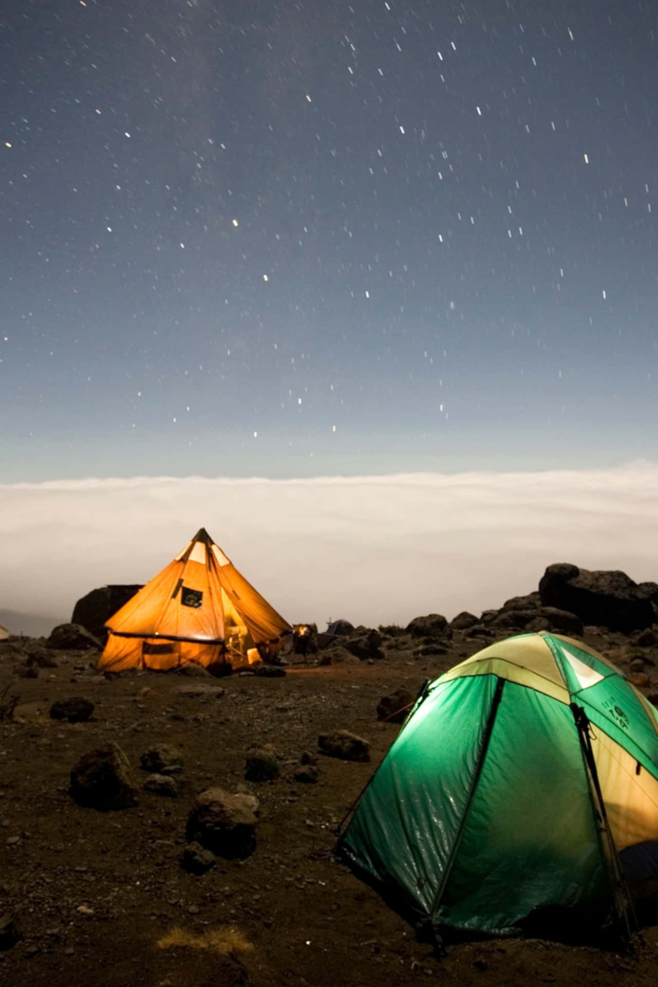 夜間山上兩個亮著的帳篷，上方有星星，下方有雲。