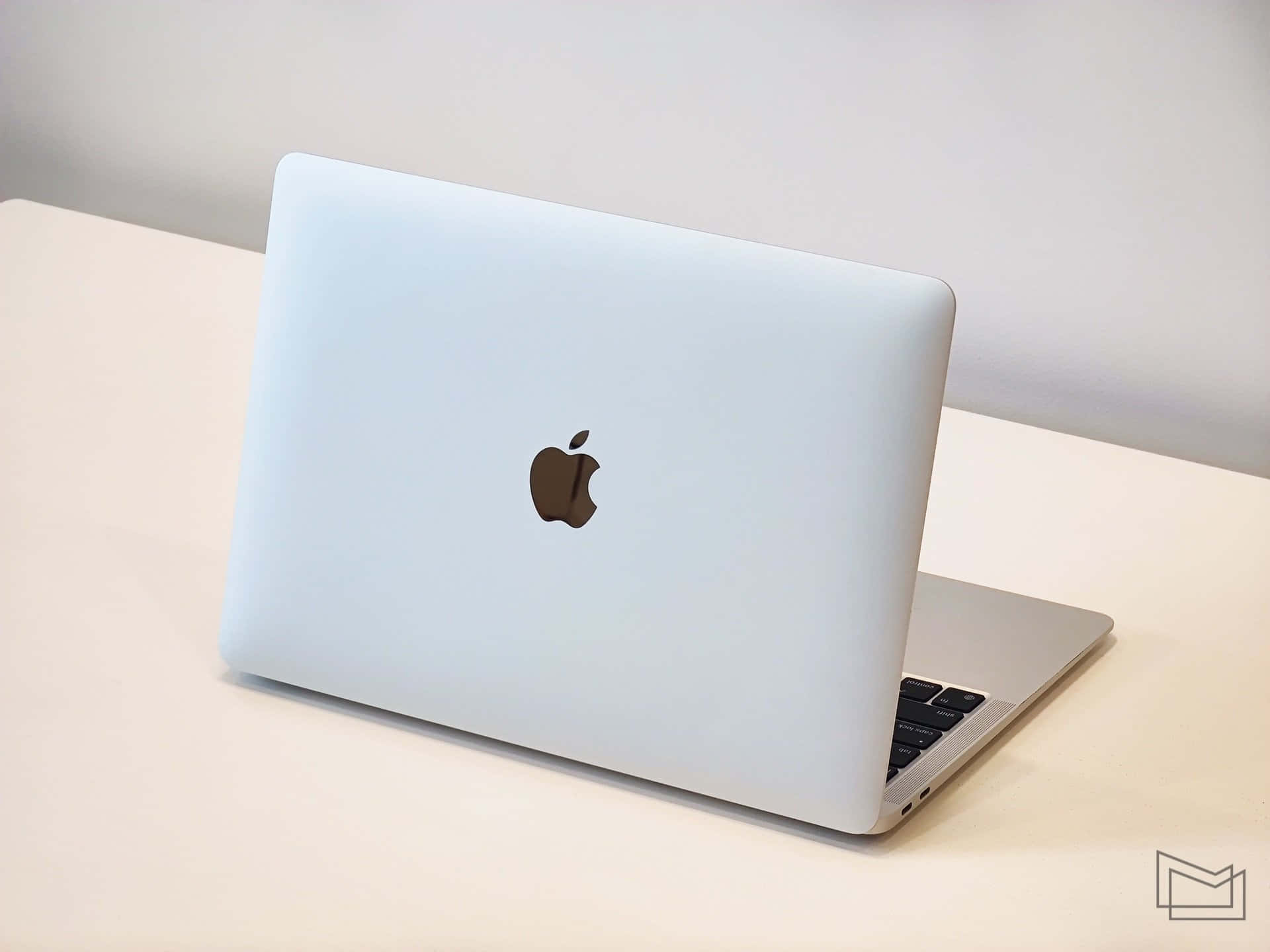在優雅自然光下工作 壁紙 — 一部時尚的銀色 MacBook 筆記型電腦在柔和日光下打開，放在簡約的白色桌子上。