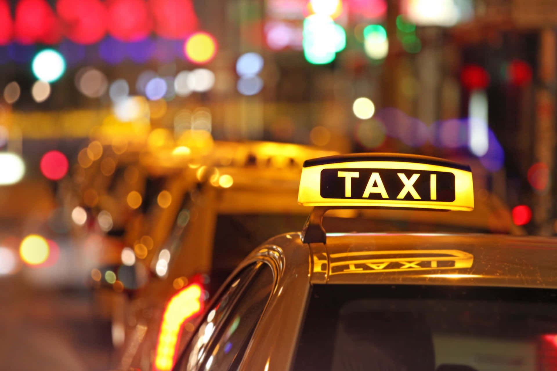 Yellow Cab 桌布 壁紙 — 在充滿活力的散景燈光城市夜景中，一輛的士頂上發光的黃色的士標誌。