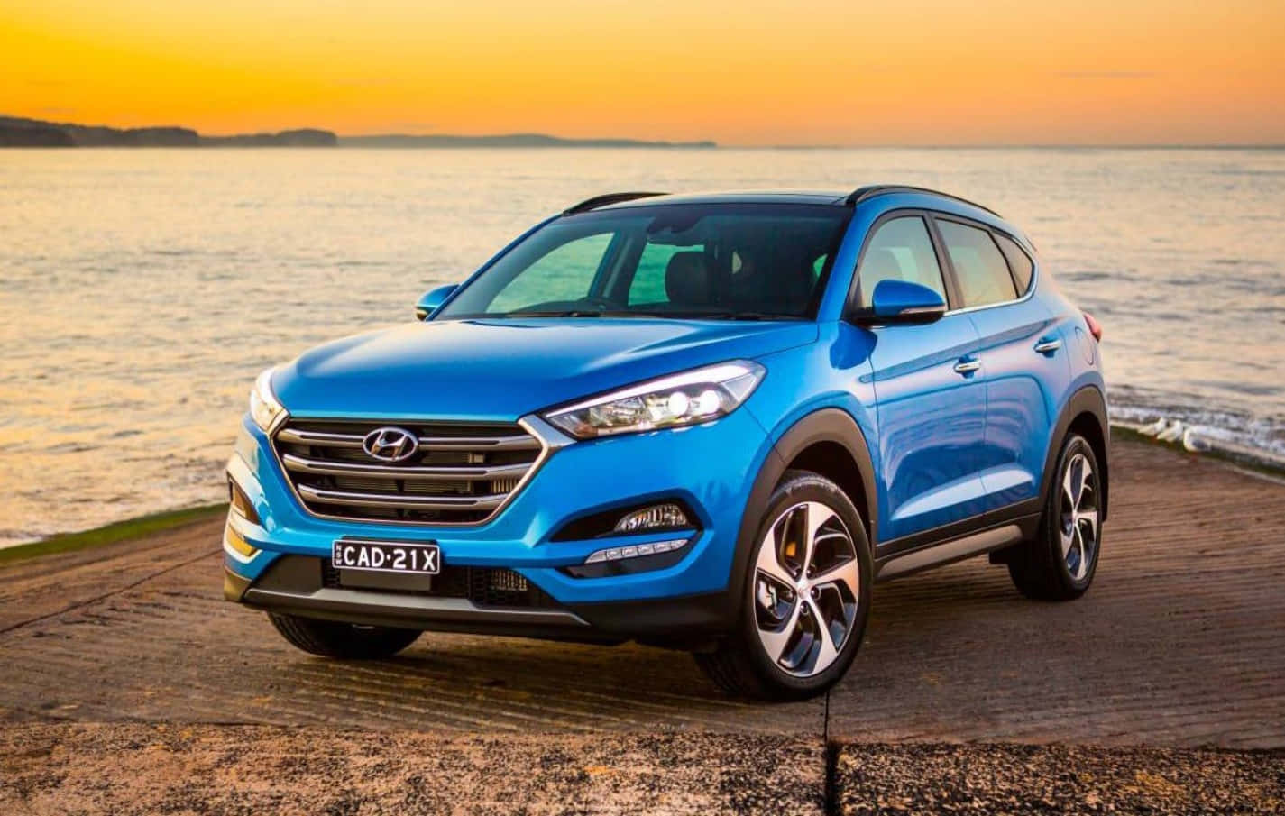 藍色現代 Tucson SUV 停泊在金色日落時分的水邊木製碼頭上。