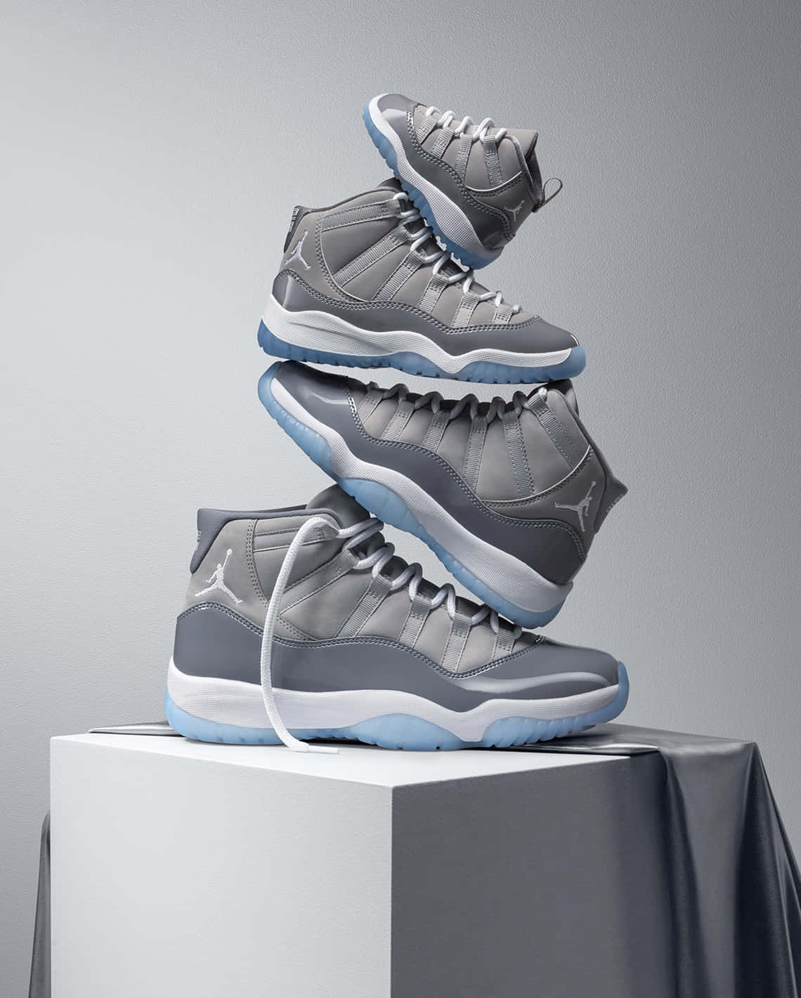 在攝影棚環境中，白色底座上堆疊的灰色 Jordan 11 運動鞋。