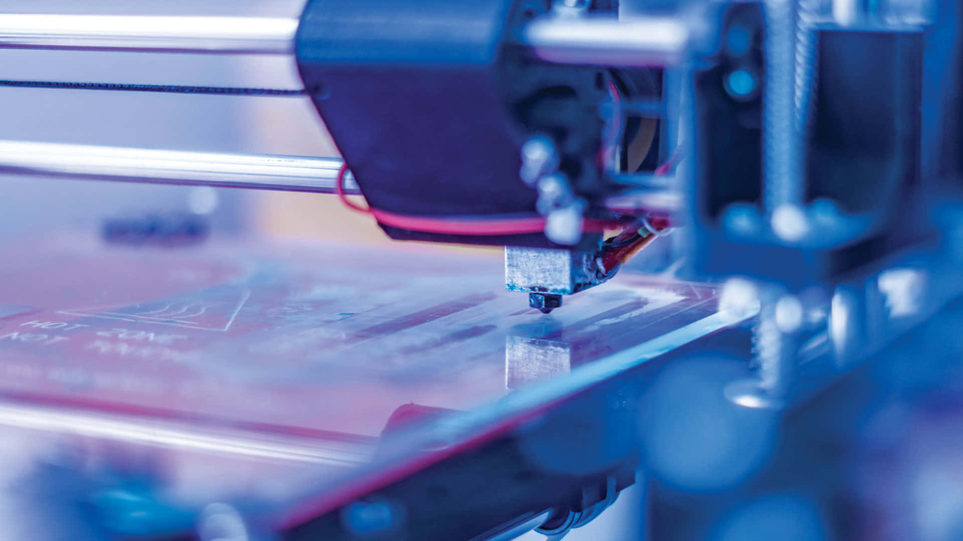 3d Printer 桌布 壁紙 — 在冷藍色燈光下，3D打印機將線材擠出到打印平台上的特寫。