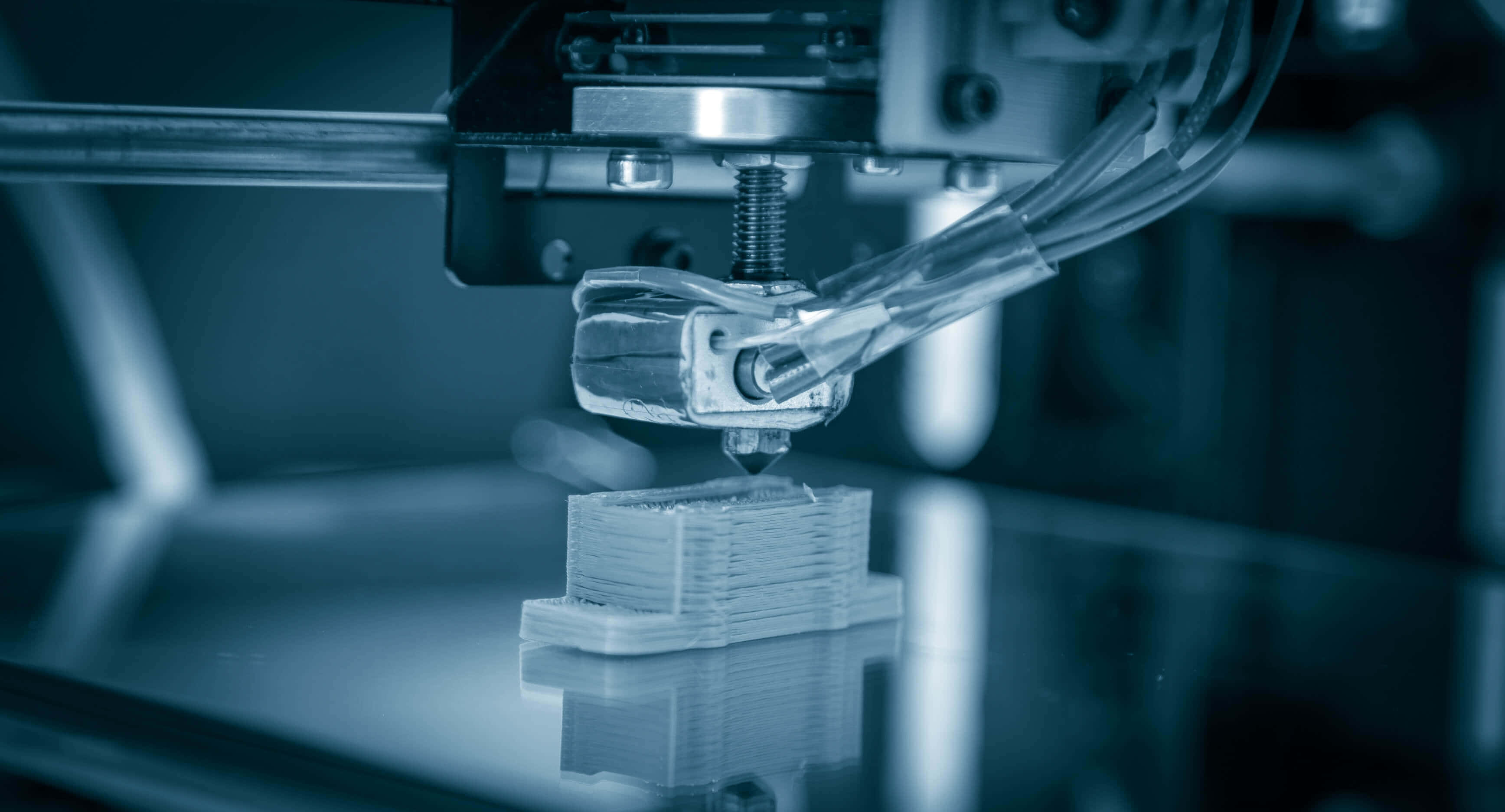 Manufacturing 桌布 壁紙 — 在冷藍色燈光下，3D打印機擠出線材以構建分層塑料物體的近距離特寫。