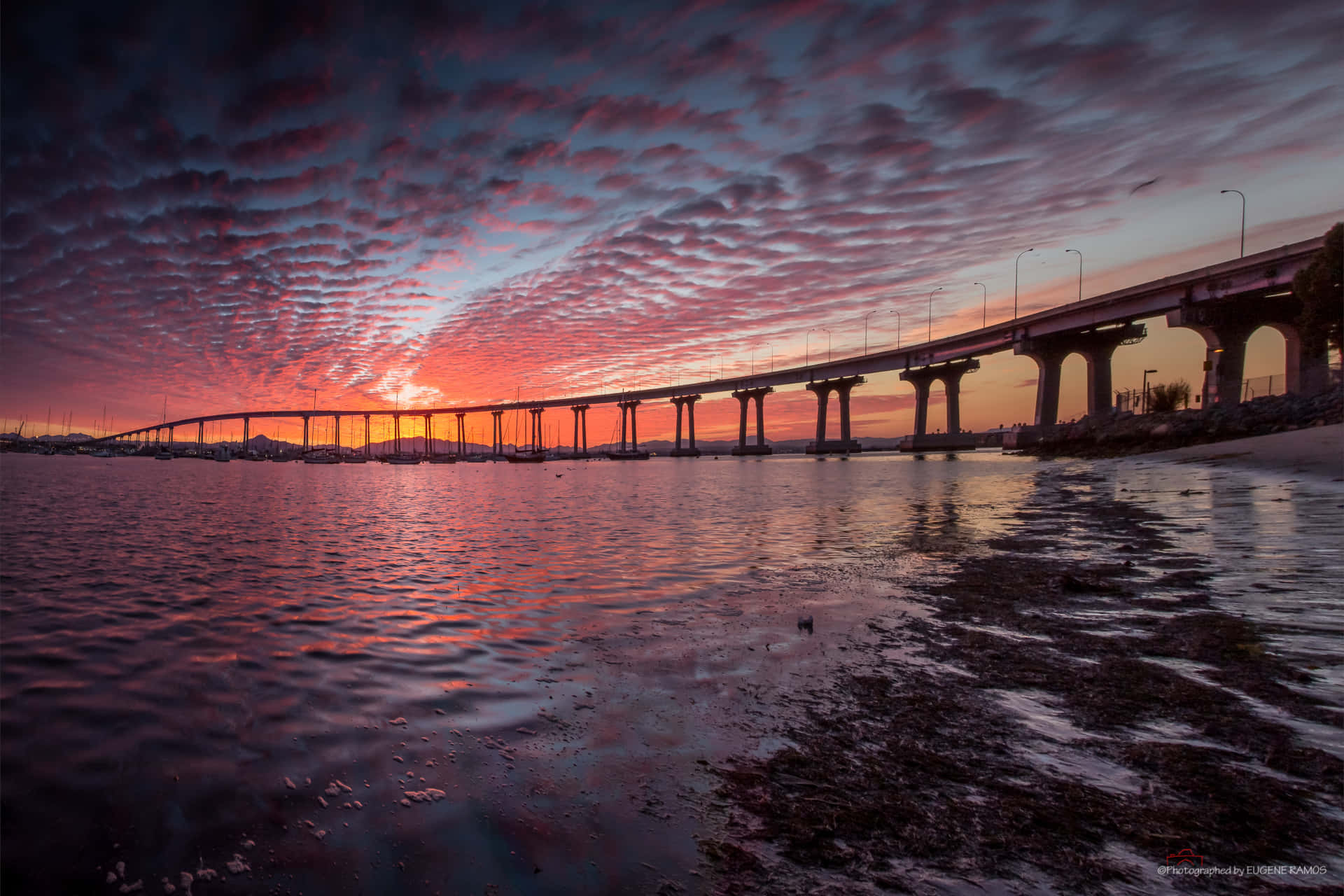 日落時分水上的長橋，色彩繽紛的雲彩倒映在水中。