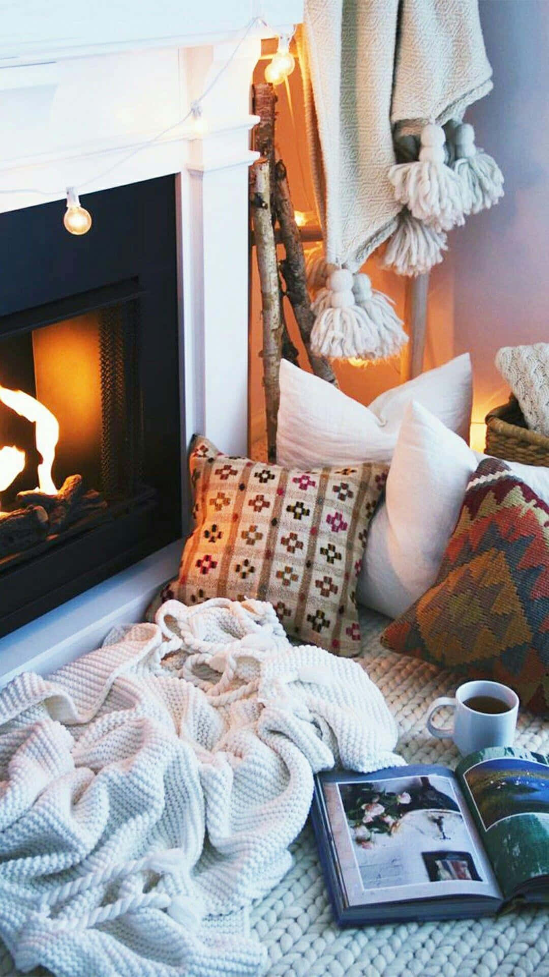 Cozy Fire 桌布 壁紙 — 在噼啪作響的壁爐旁，一個舒適的閱讀角落，配有針織毯子、圖案抱枕和散發溫暖光芒的串燈。